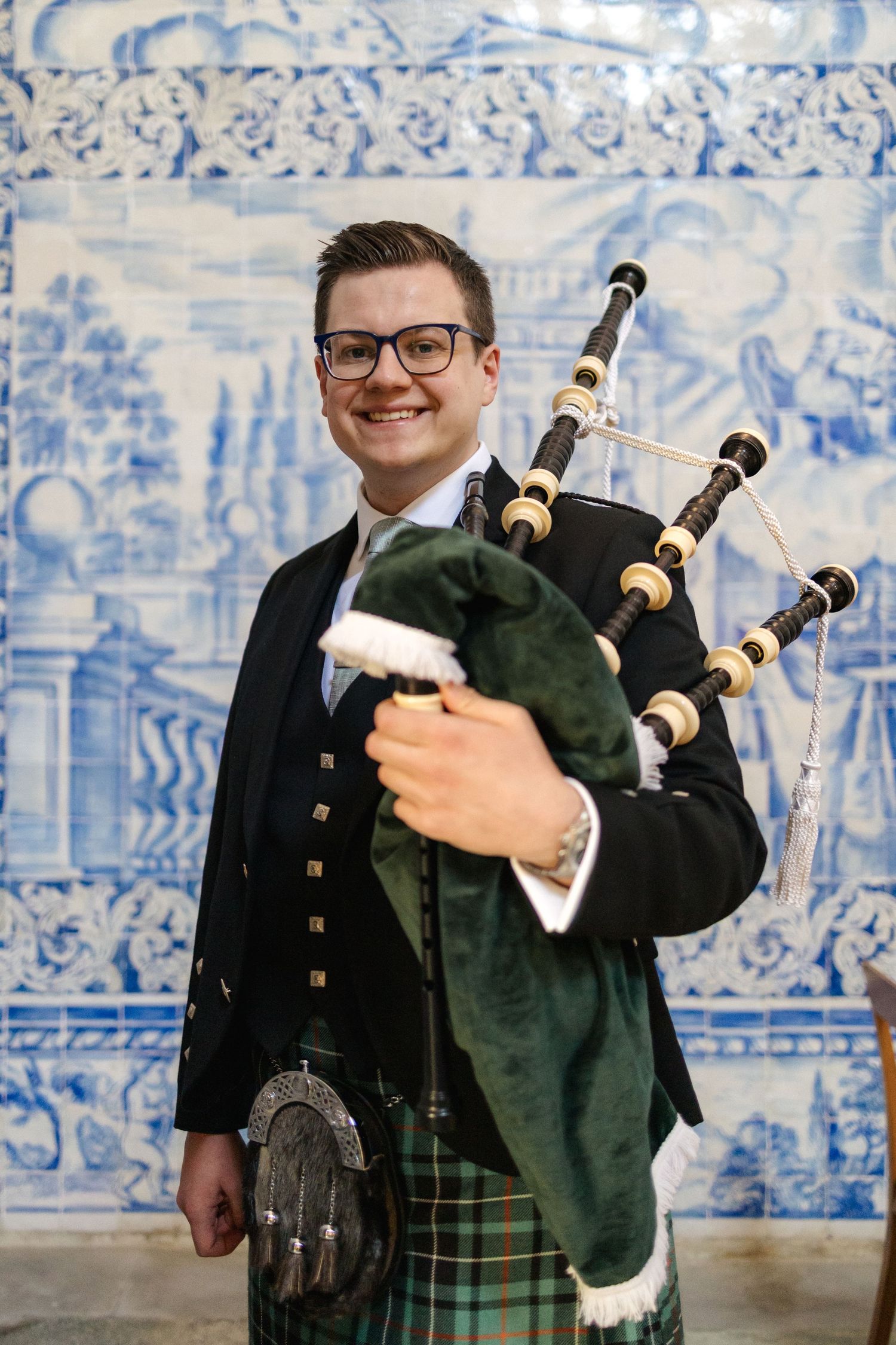 Musician holds bagpipes against a backdrop of blue and white Portuguese azulejo tiles.