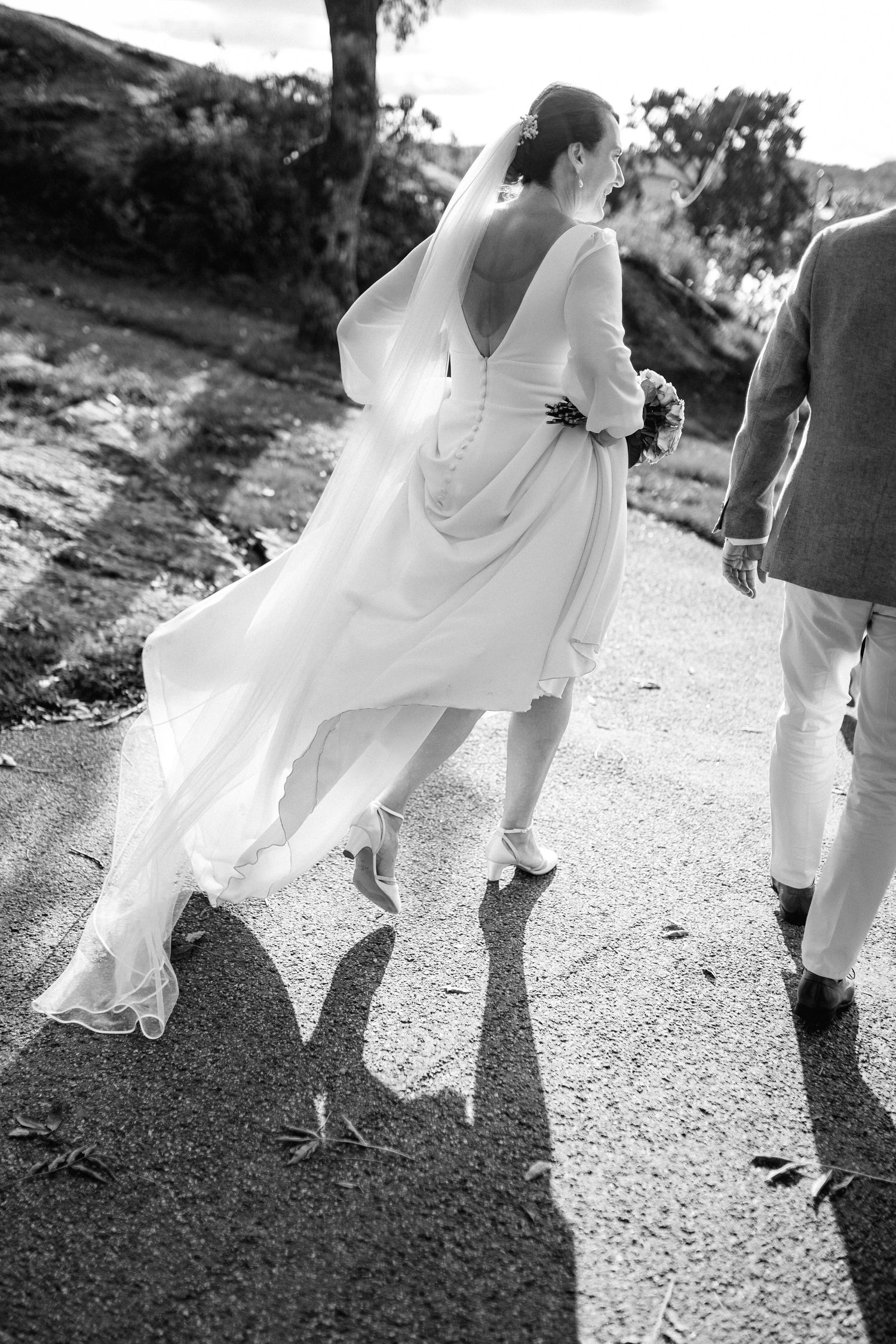 Black and white photo showing flowing white dress and feet walking on a gravel path.