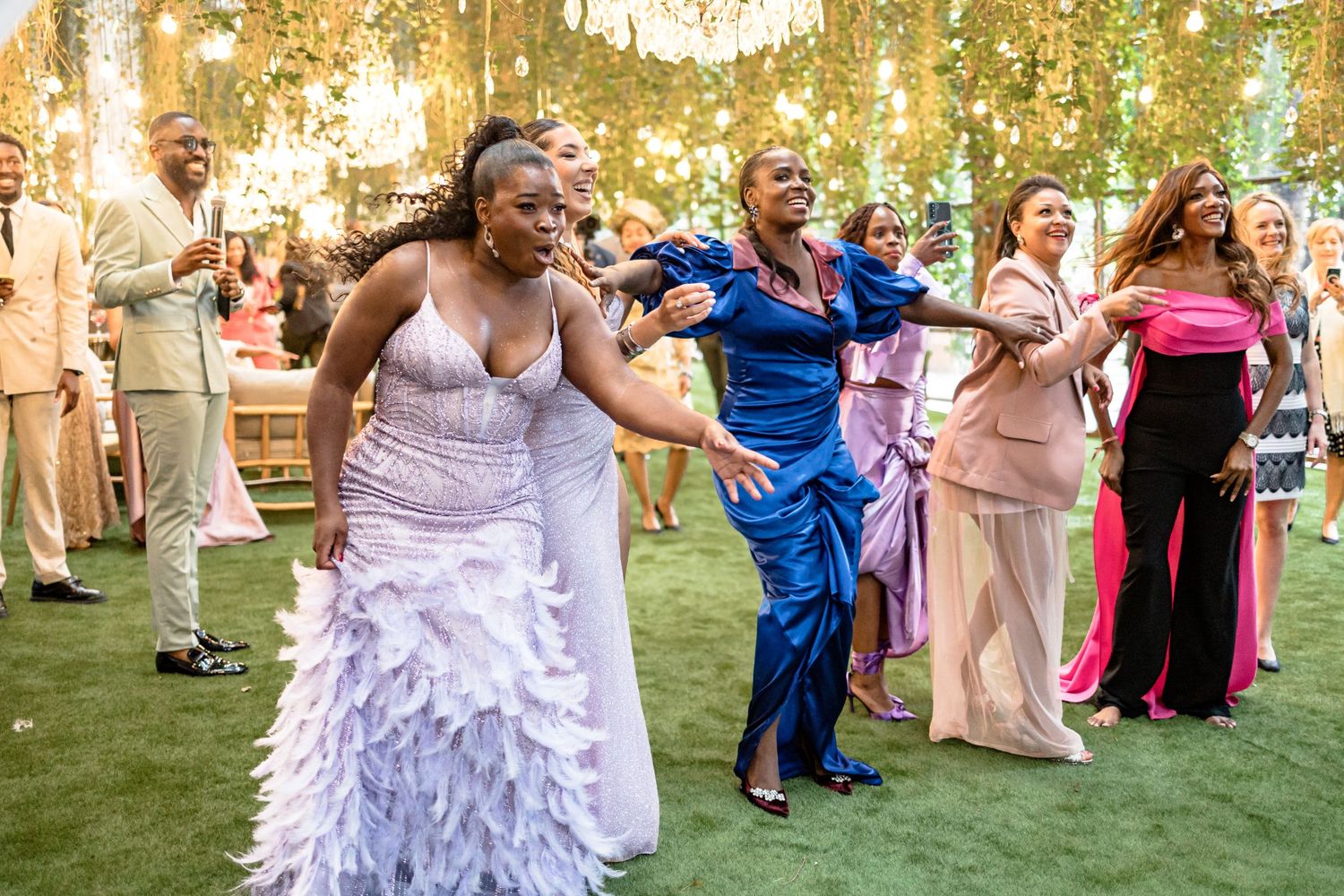Wedding reception guests dancing and celebrating under hanging garden lights.