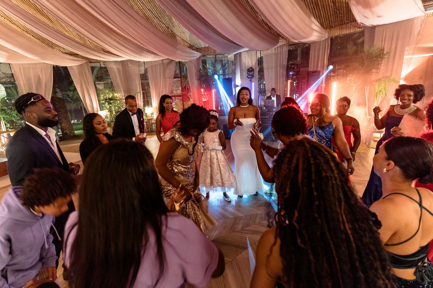 Guests enjoying themselves at an indoor wedding reception with pink lighting and draped fabric decor.