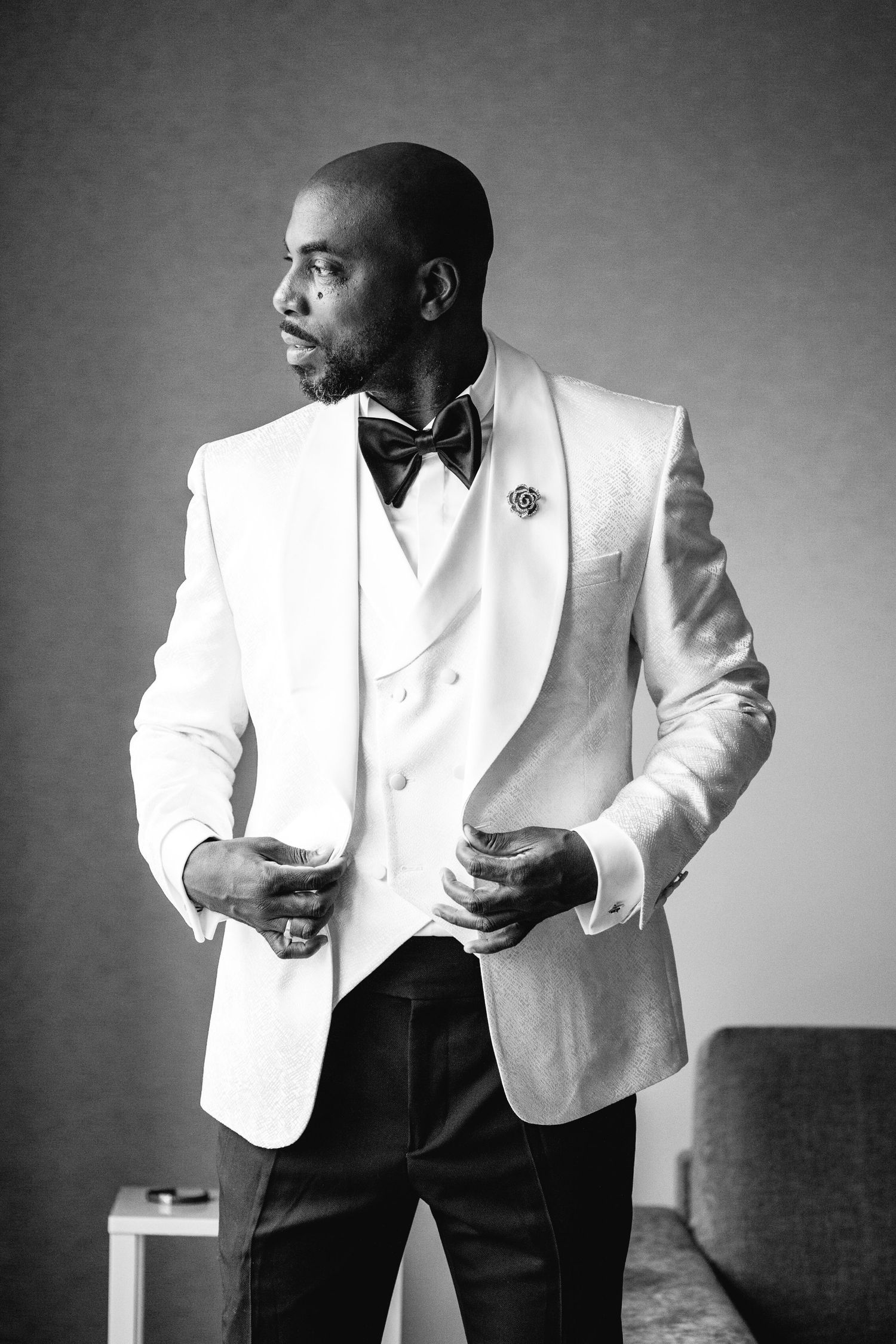 Black and white portraits of groom in crisp white tuxedo jacket and bow tie striking dynamic poses.
