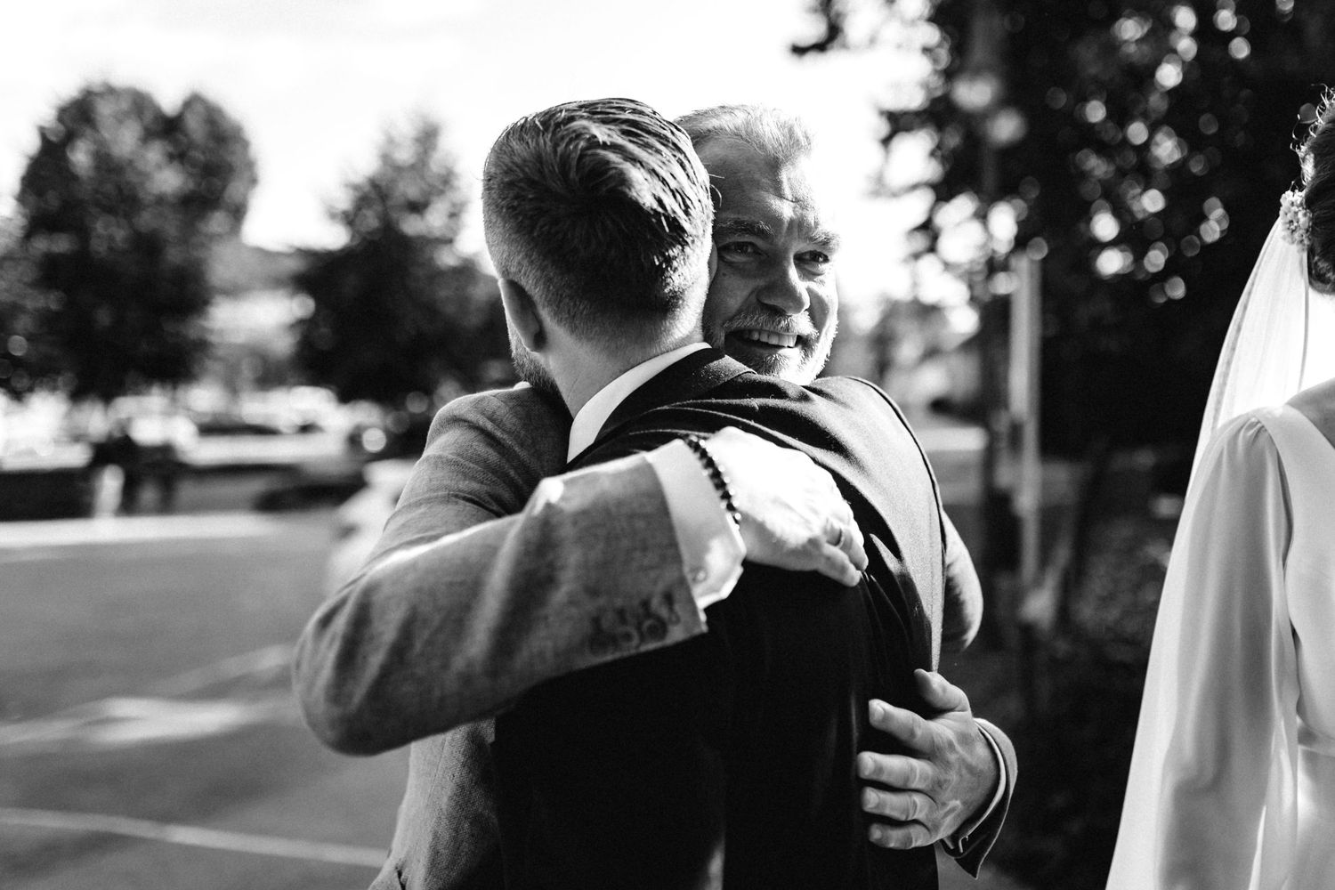 Two wedding guests share an emotional embrace outdoors on a sunny day.