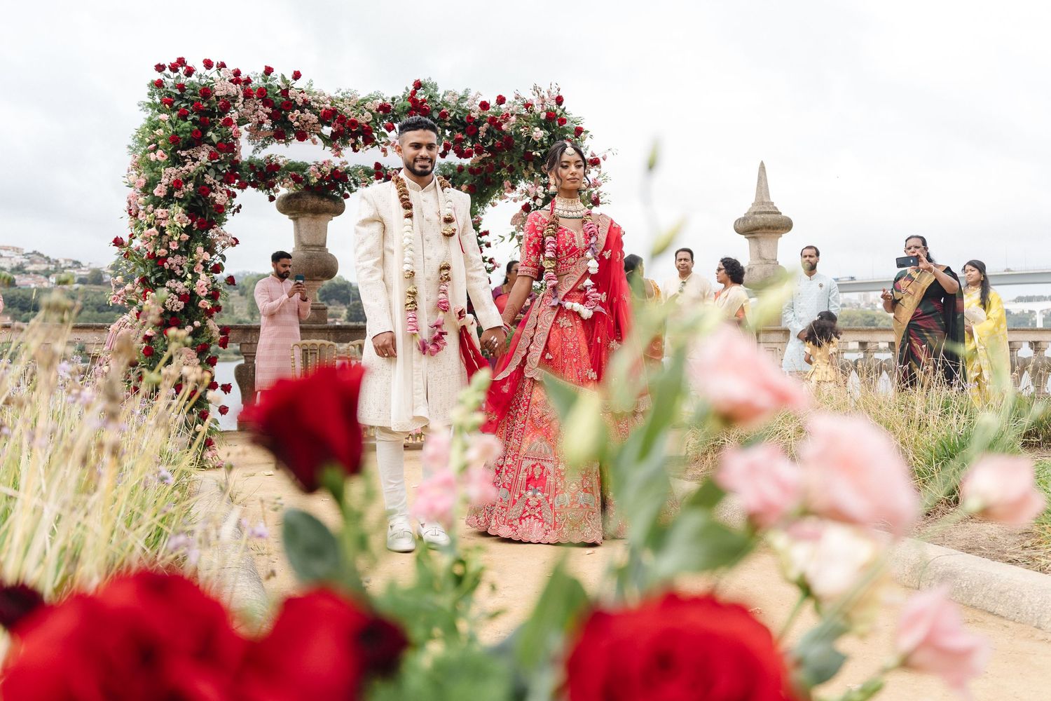 Outdoor celebration under an elaborate arch of red and pink flowers.