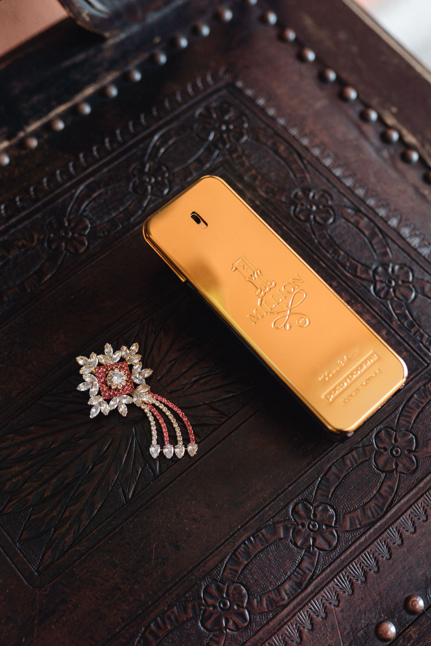Gold perfume bottle and crystal jewelry arranged on dark embossed leather surface.