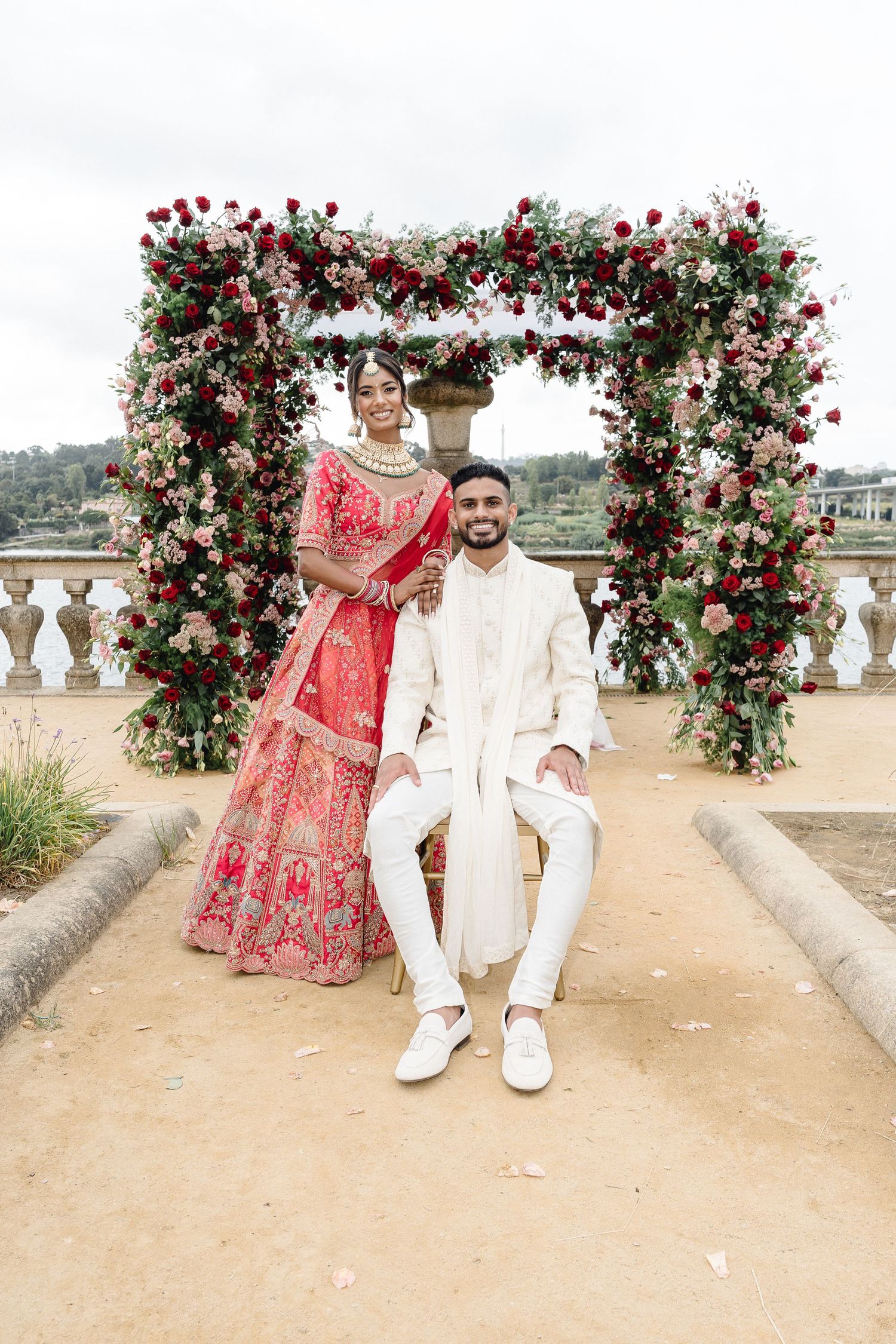 Romantic wedding portraits under red rose floral arches at an elegant outdoor venue.