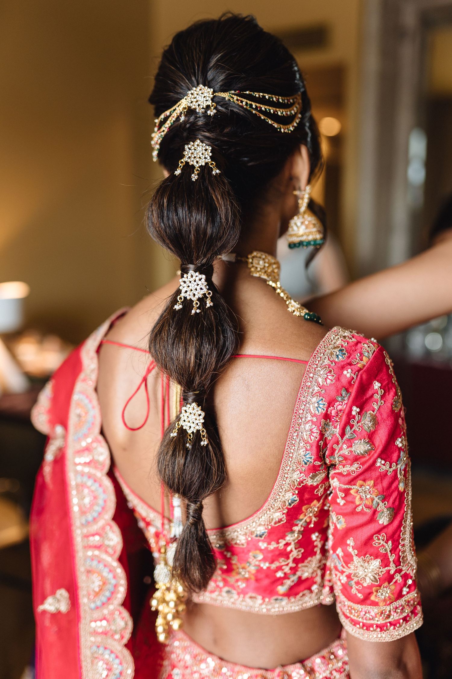 Back view of traditional red Indian bridal outfit with detailed embroidery and hair accessories.