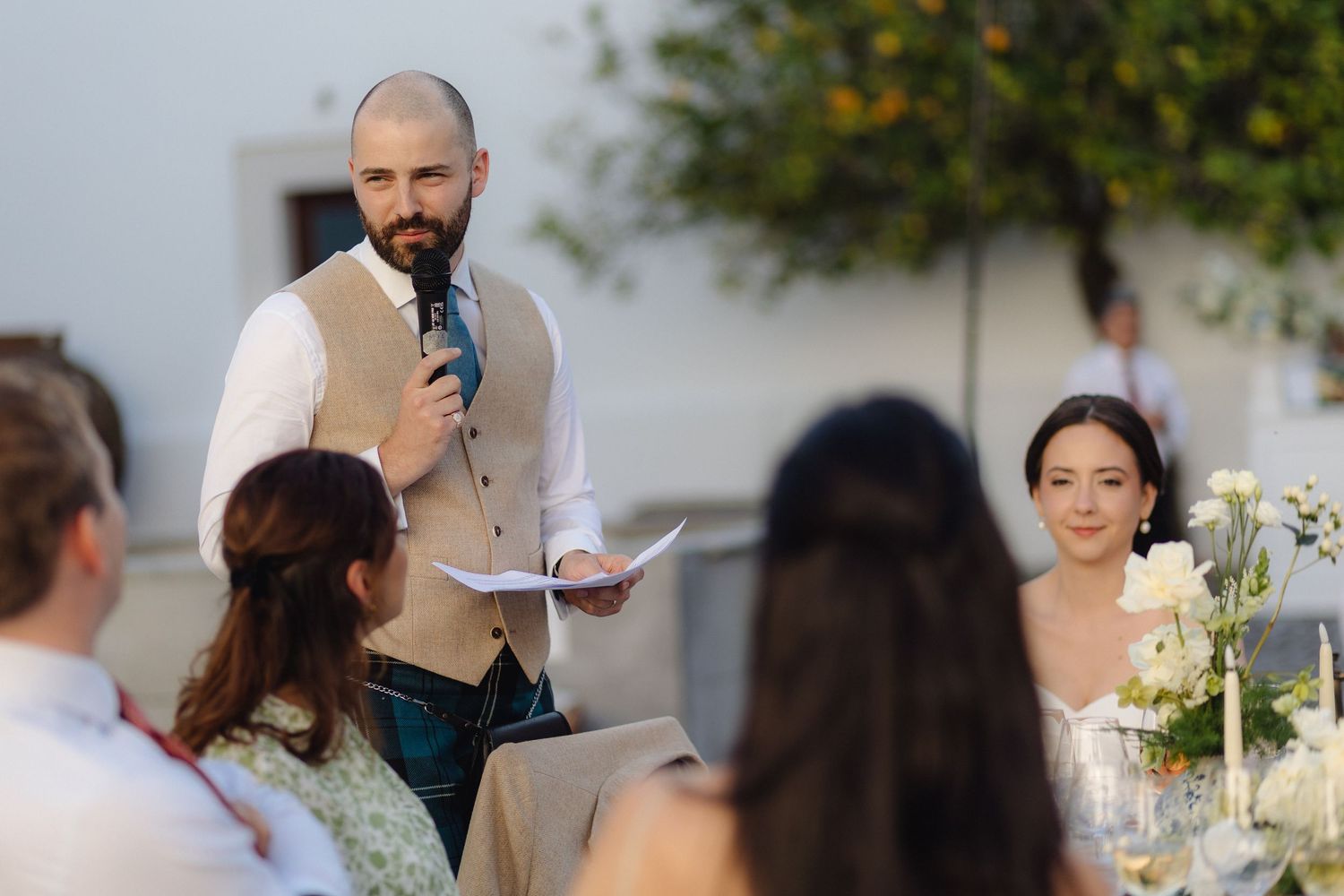 A speaker addresses guests at an outdoor wedding reception.