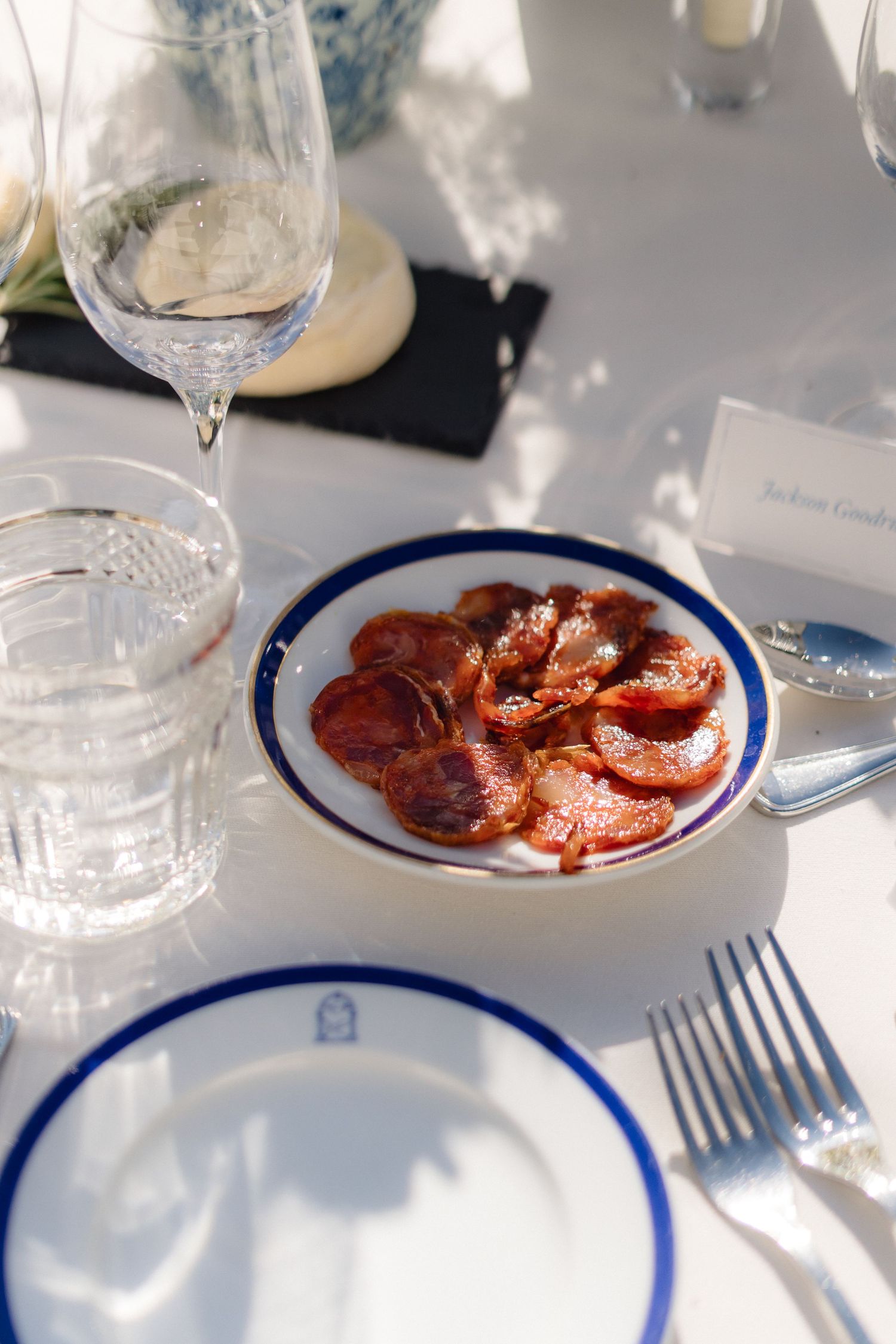 Plate of sliced cured meats served with blue-rimmed dinnerware and wine glasses.