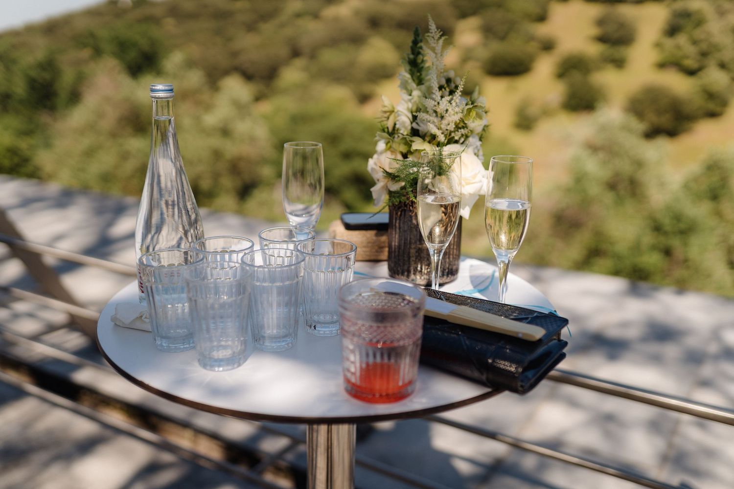 An elegant table setting with champagne glasses and floral arrangements against a scenic hillside view.