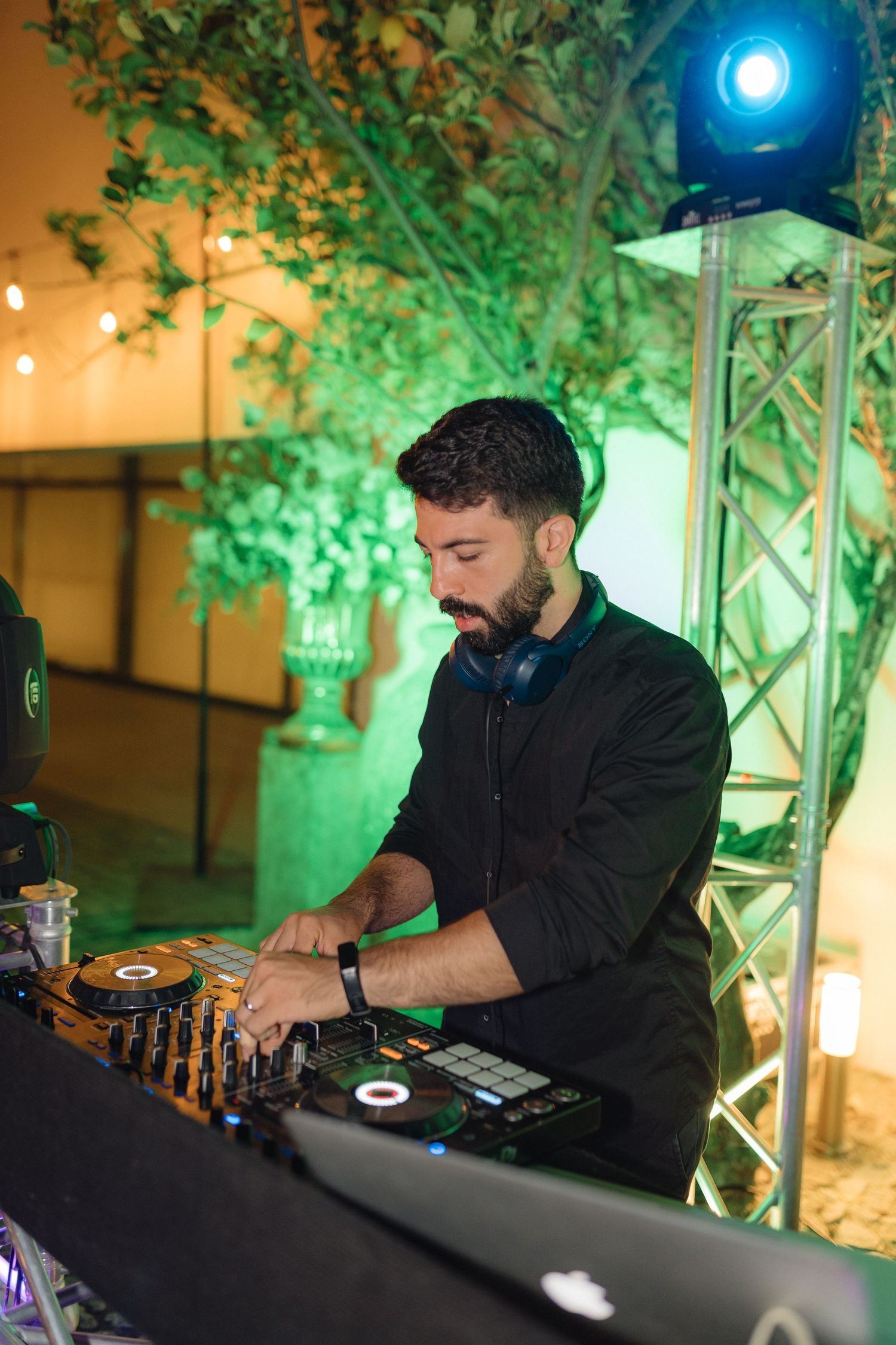 DJ performing at an event with professional equipment under green ambient lighting.