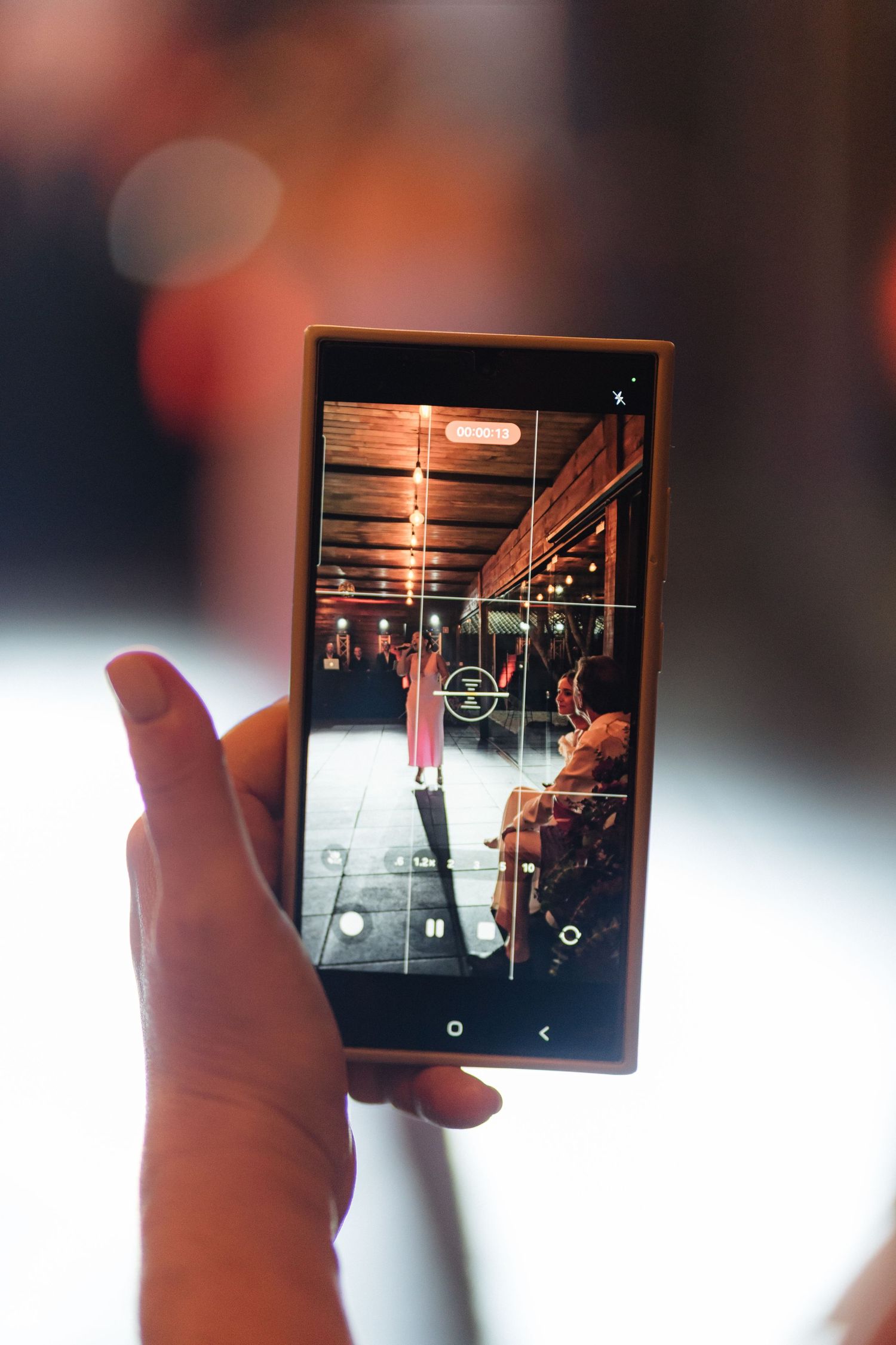 A hand holds up a phone capturing a performance through its screen at an indoor venue.