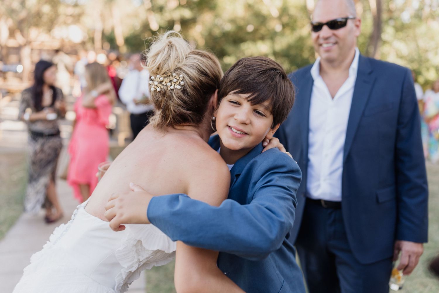 Wedding guests celebrate with laughter and hugs in a sunny outdoor setting.