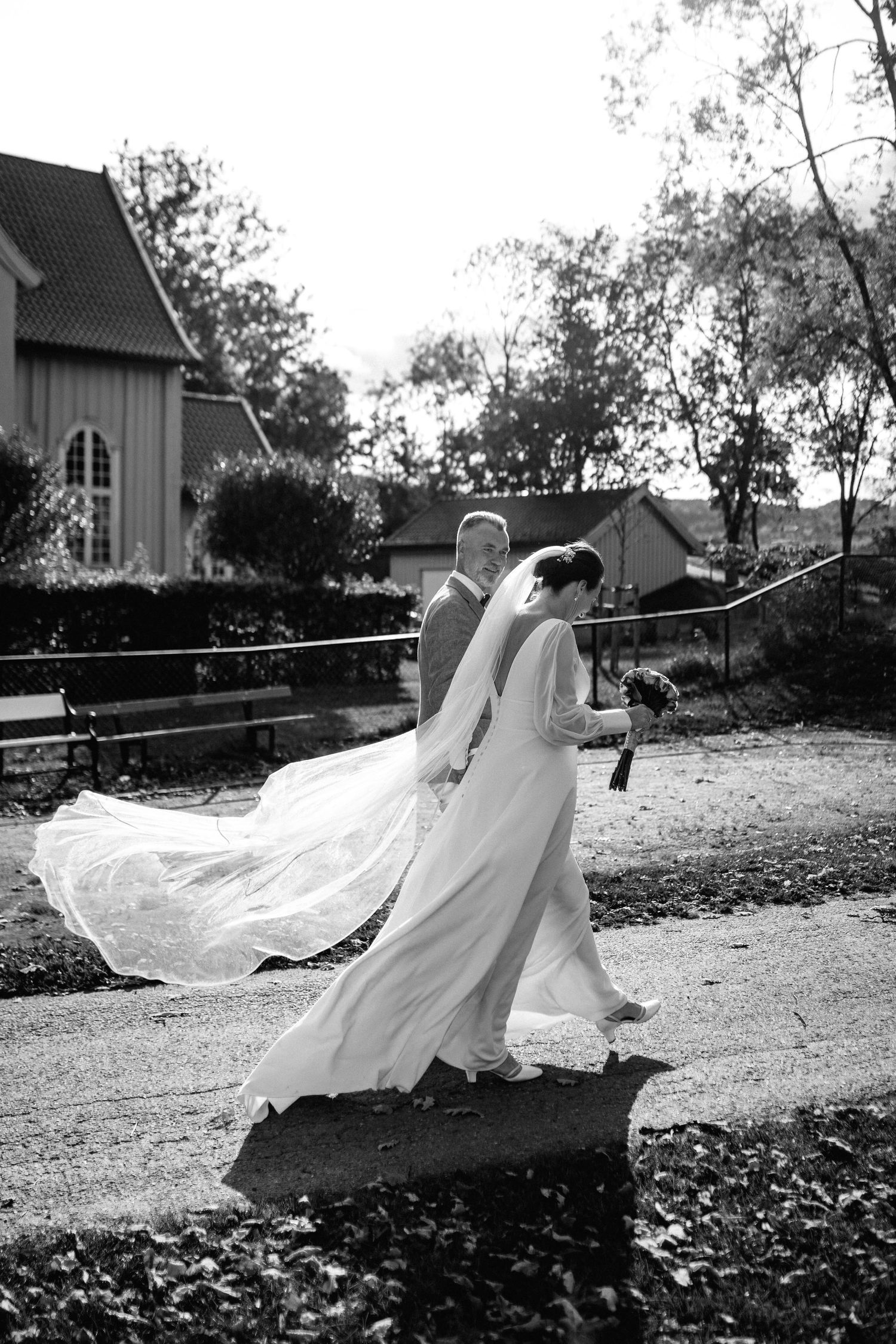 A wedding dress flows dramatically in the wind against a rustic church backdrop.