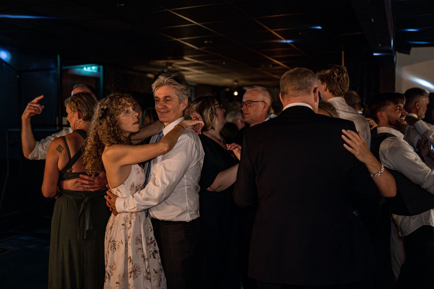 Wedding party dancing in a dark reception venue with atmospheric lighting.