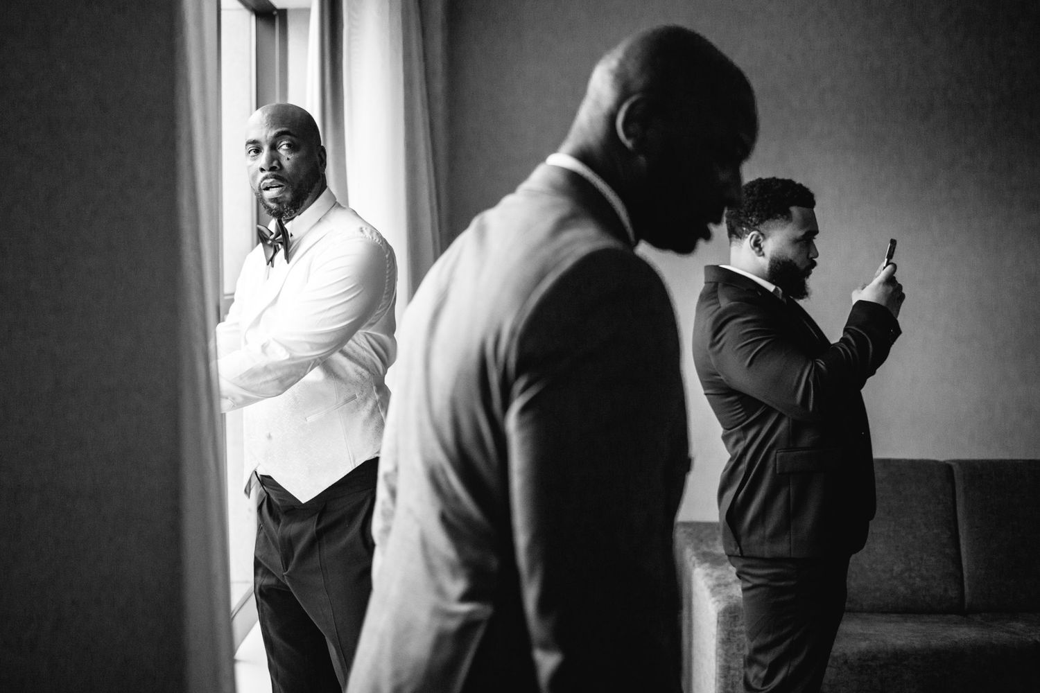 Black and white silhouettes of groomsmen getting ready by a window.
