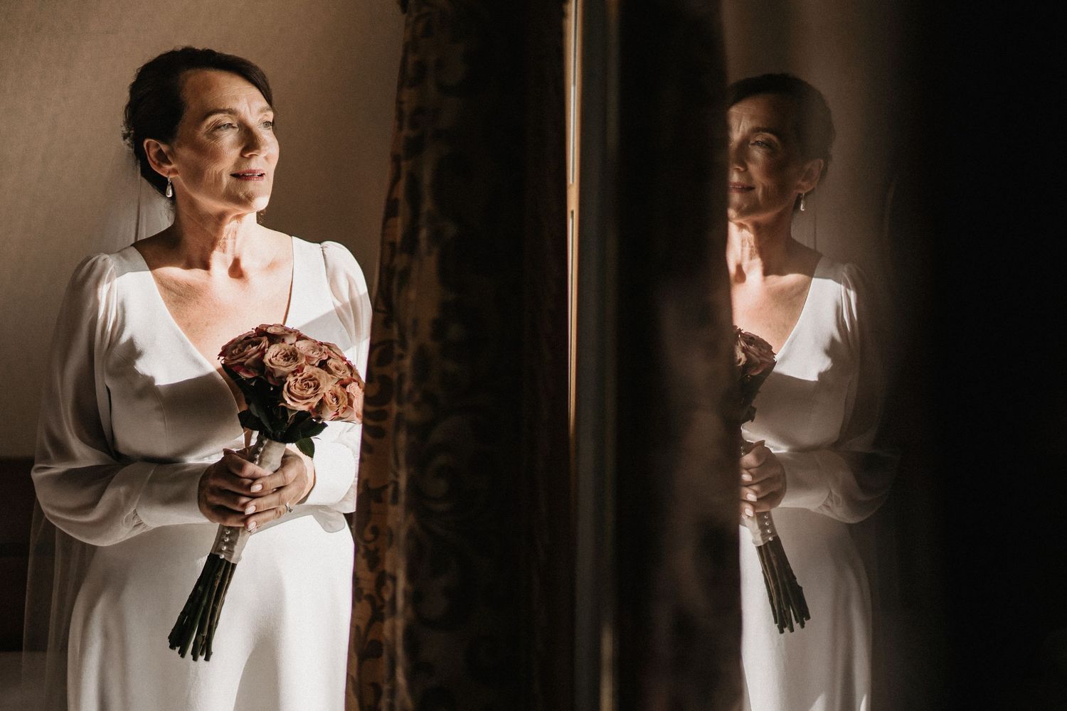 Elegant bridal portraits captured in dramatic window lighting with white robe.