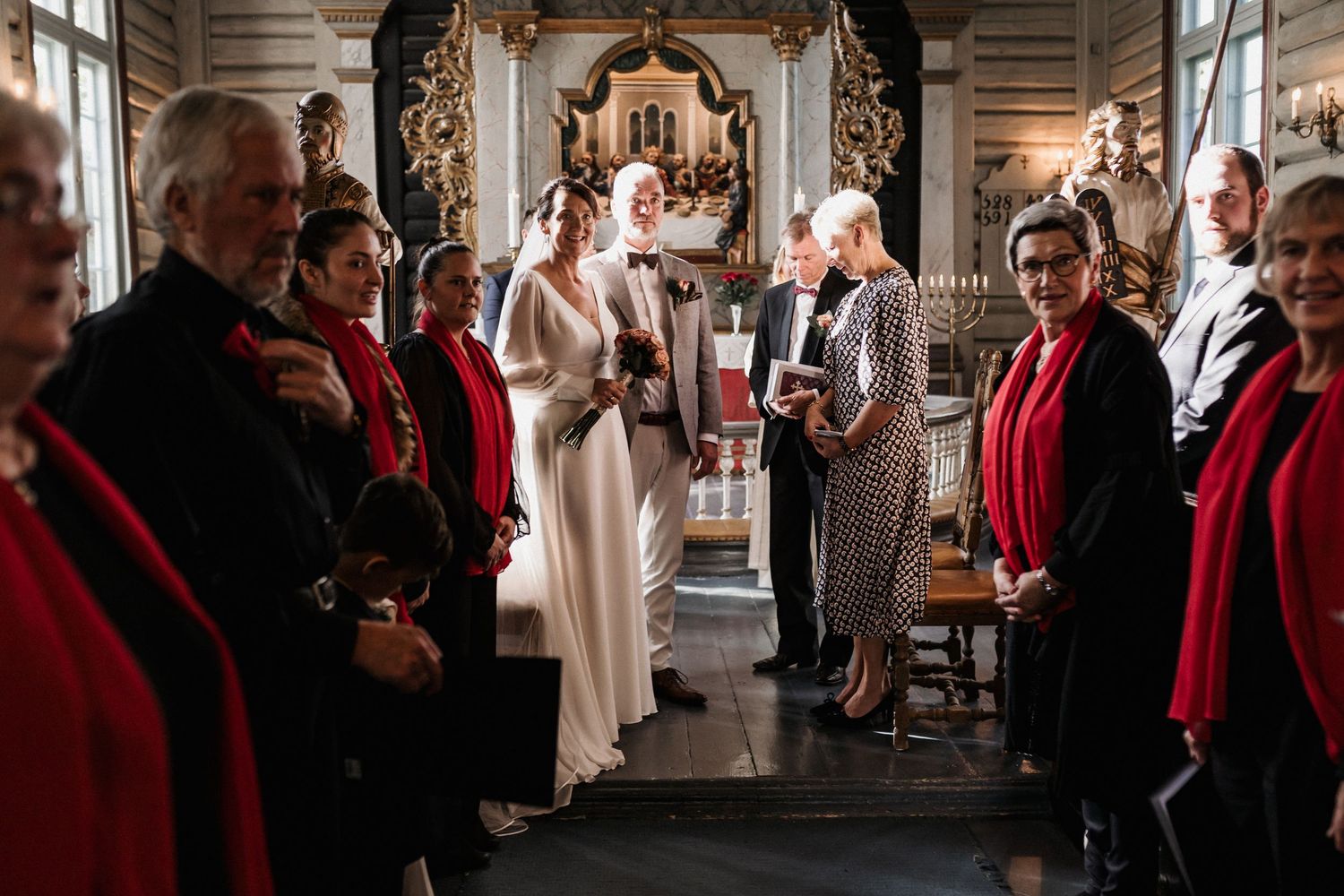 Wedding guests gather in a historic church hallway decorated with ornate details and red accents.