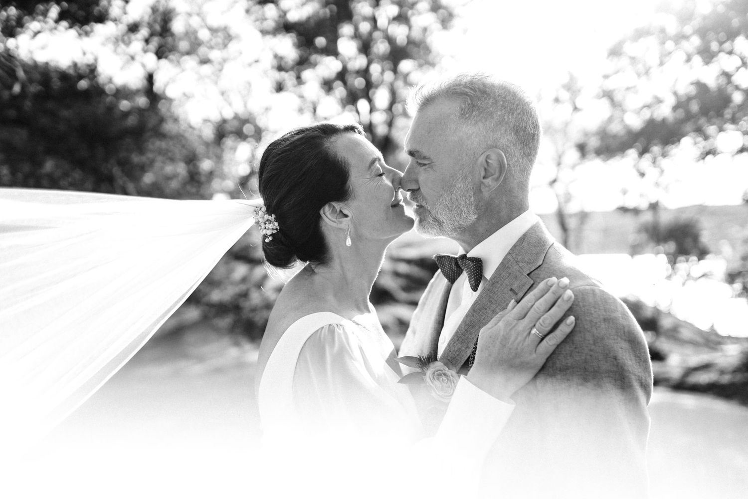 A romantic black and white wedding photo of a couple sharing an intimate moment outdoors.