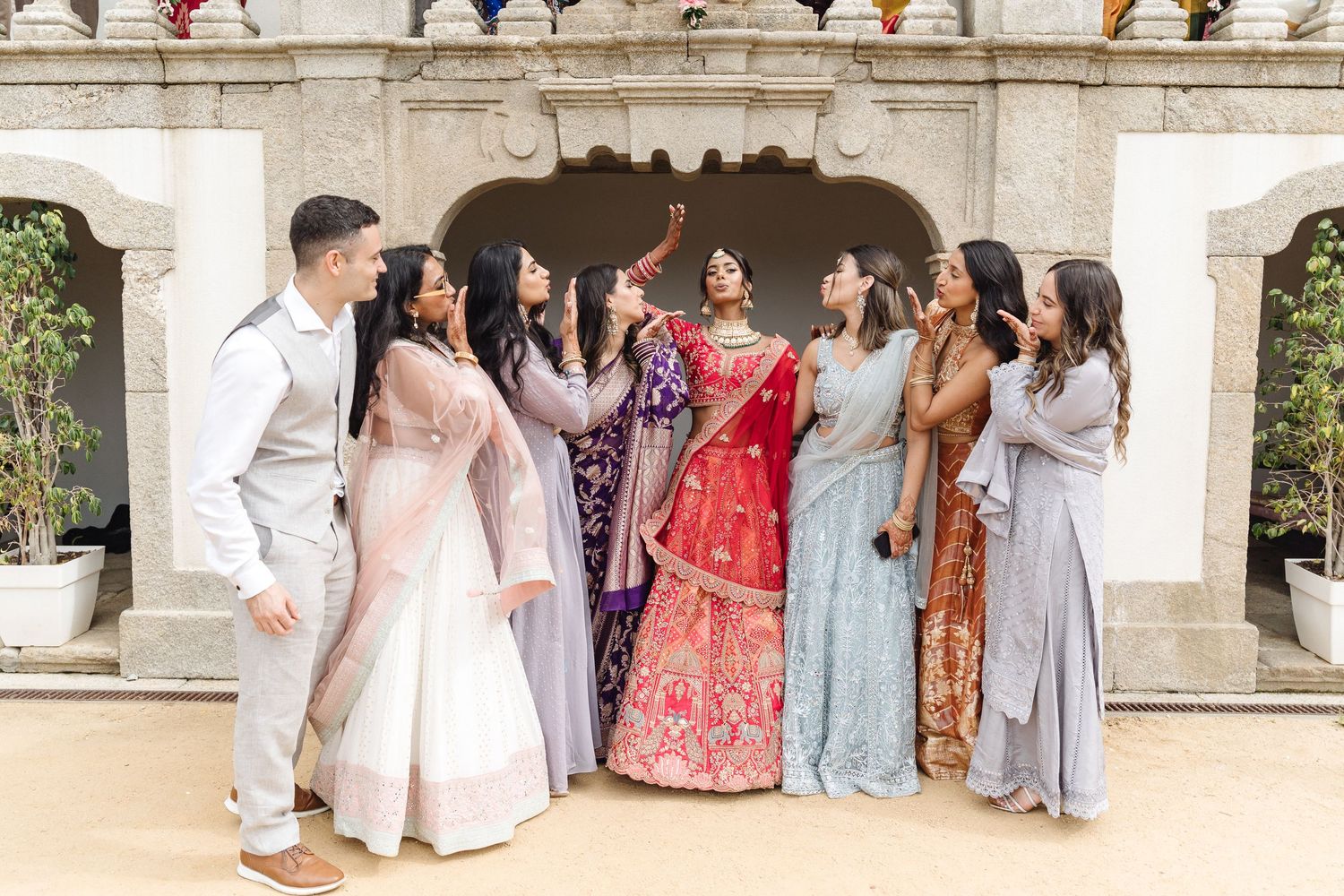 Wedding party posing in formal attire on stone steps of elegant venue.