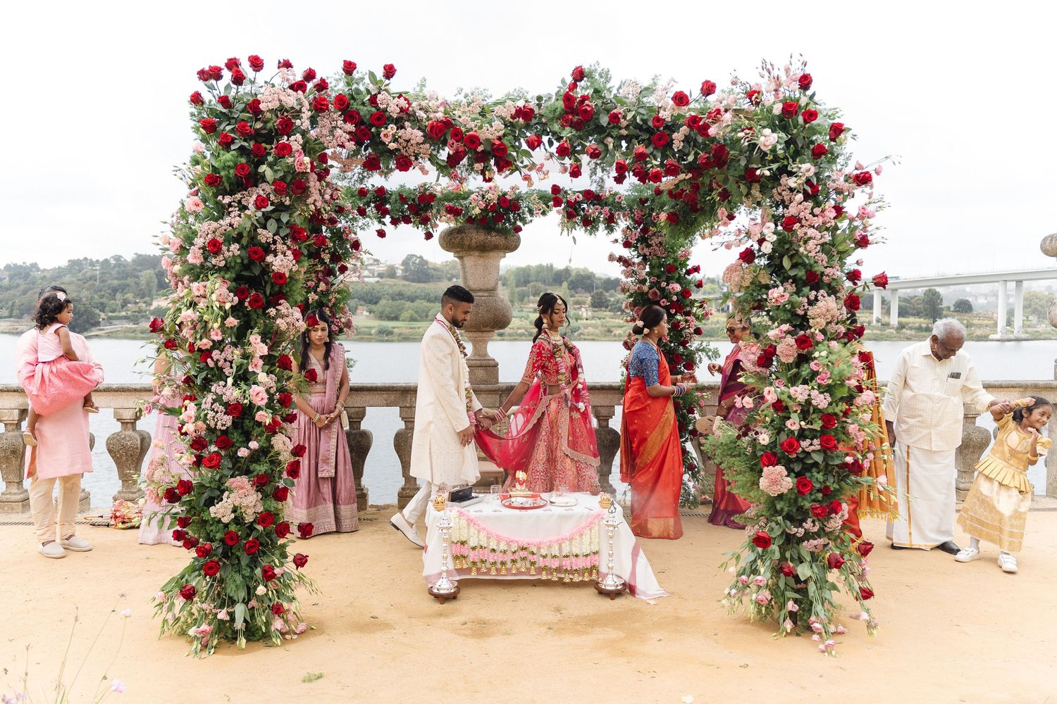 Panoramic view of a wedding venue decorated with red rose floral arches along a beachfront.