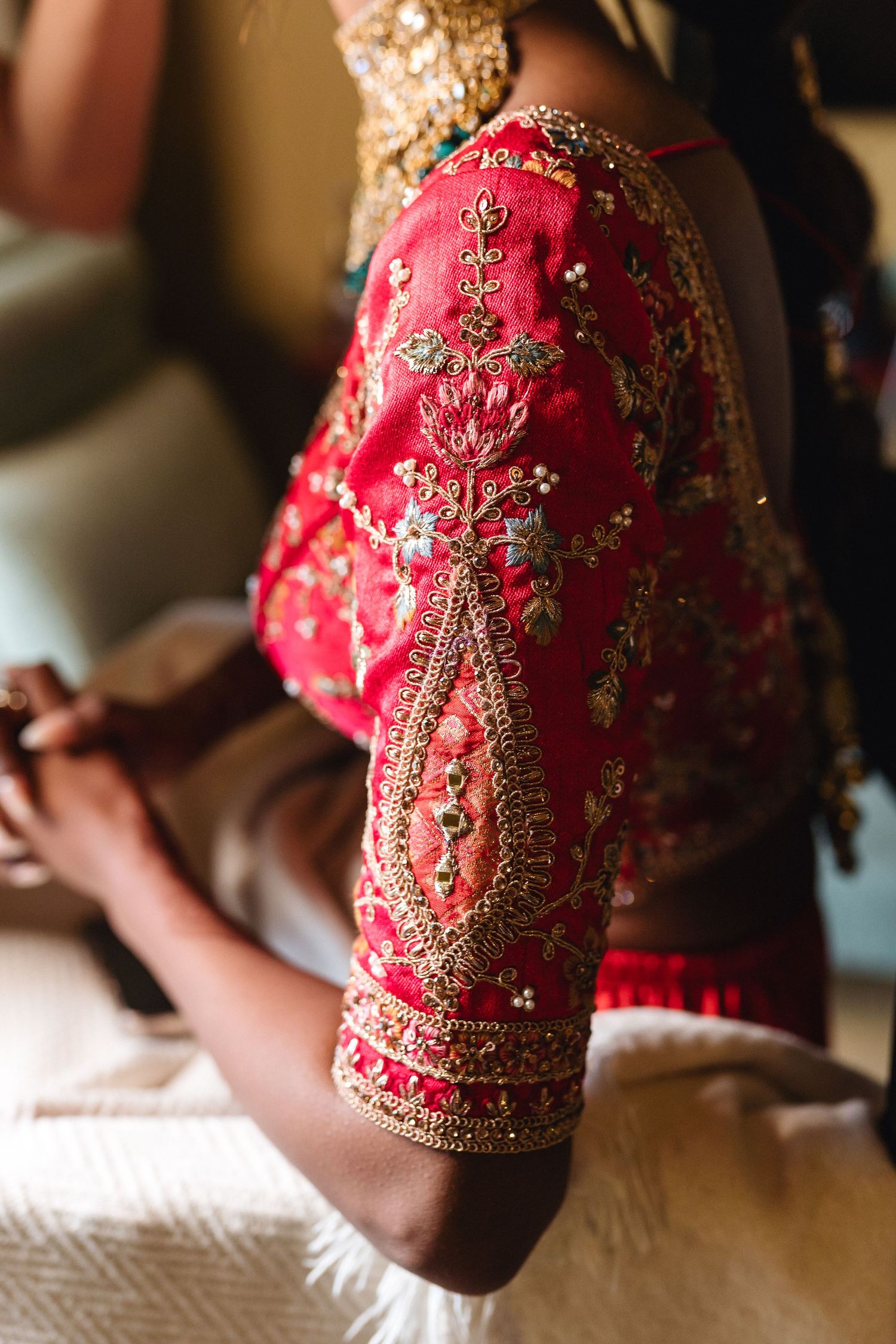 Close-up detail of an ornate red and gold embroidered sleeve from a traditional Indian wedding dress.