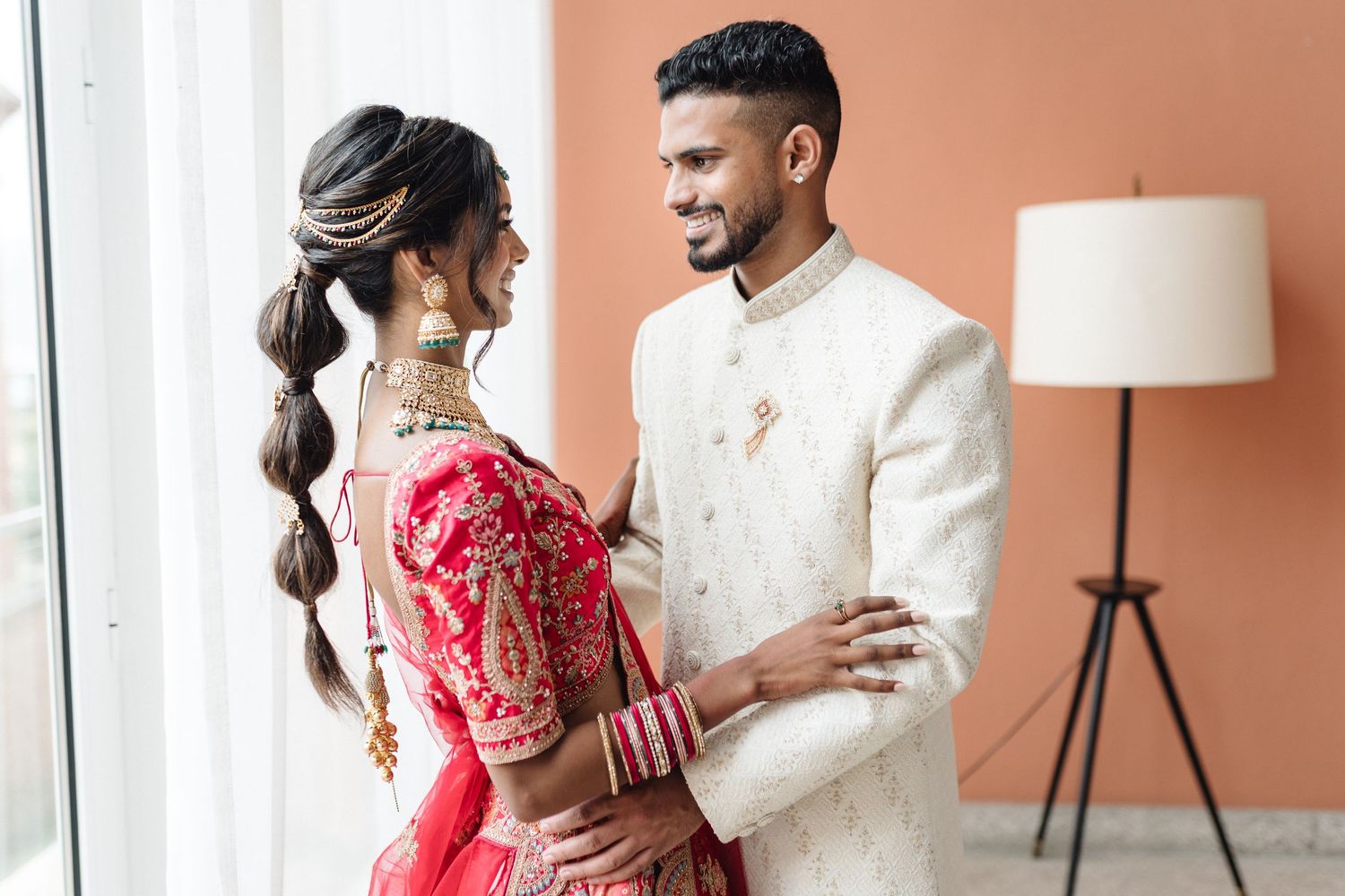Couple in formal attire sharing intimate moments against a coral-colored wall with modern decor.