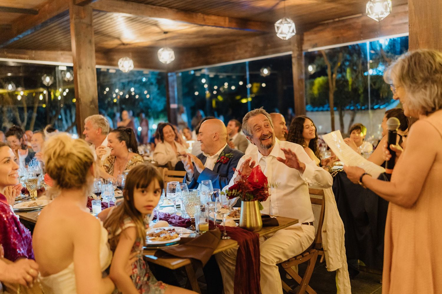 Wide angle view of a rustic reception venue with wooden beams and hanging lights.