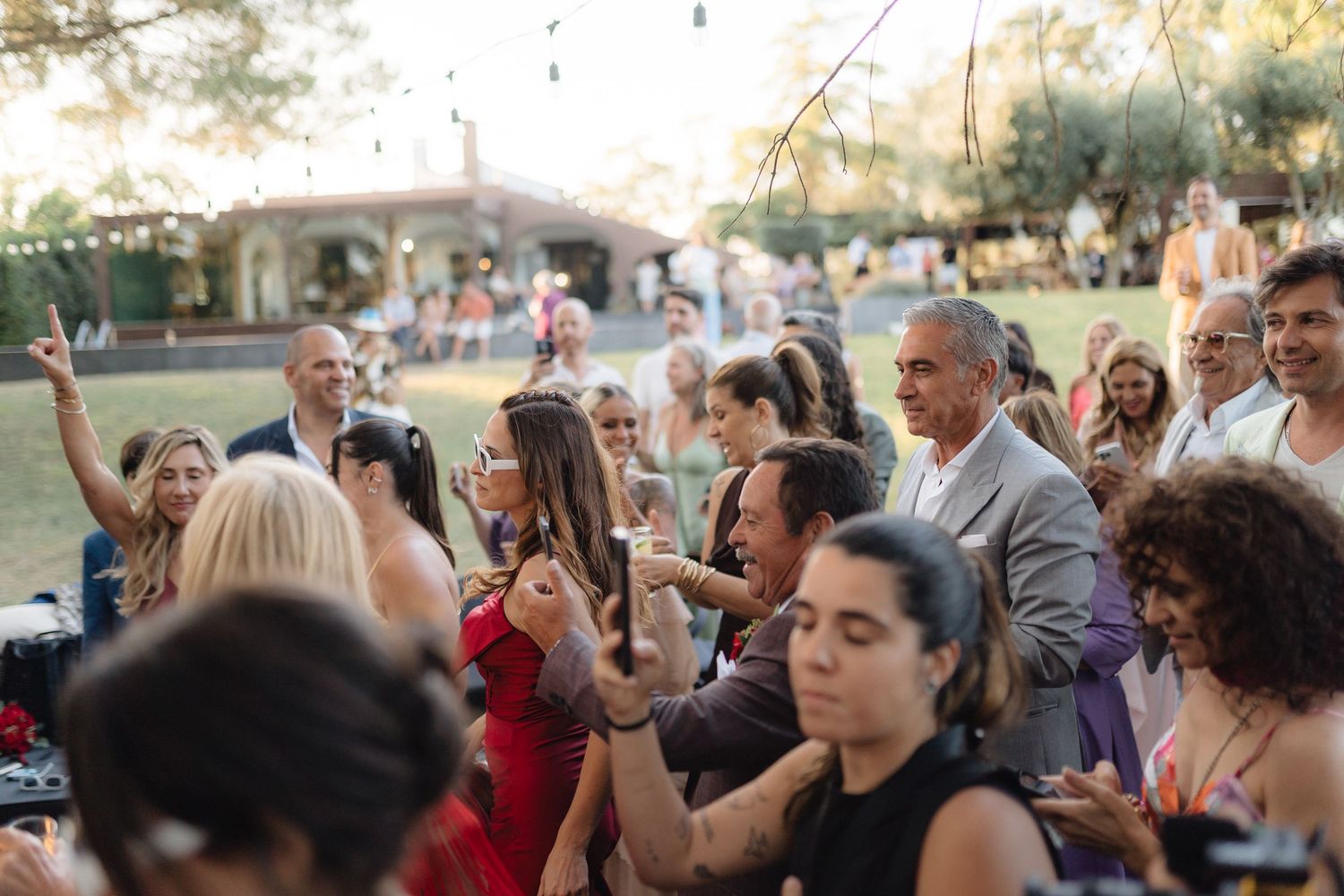Enthusiastic crowd dancing and celebrating at outdoor wedding reception.