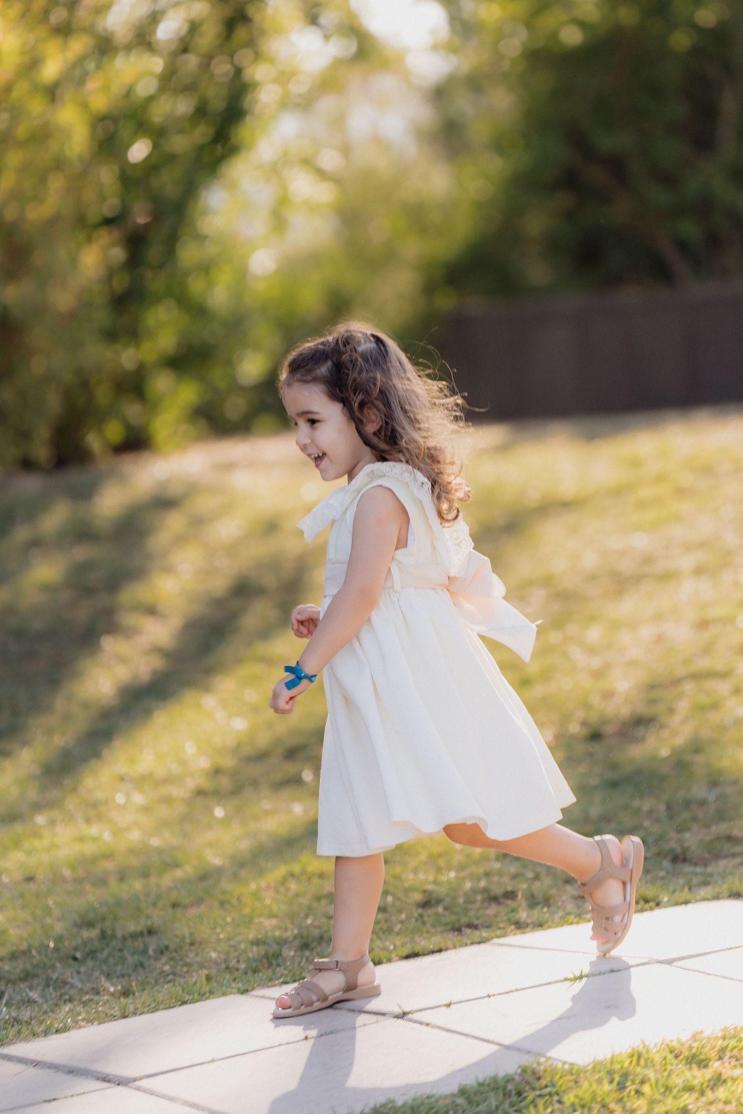 A young girl in a white dress skips along a path during an outdoor celebration.