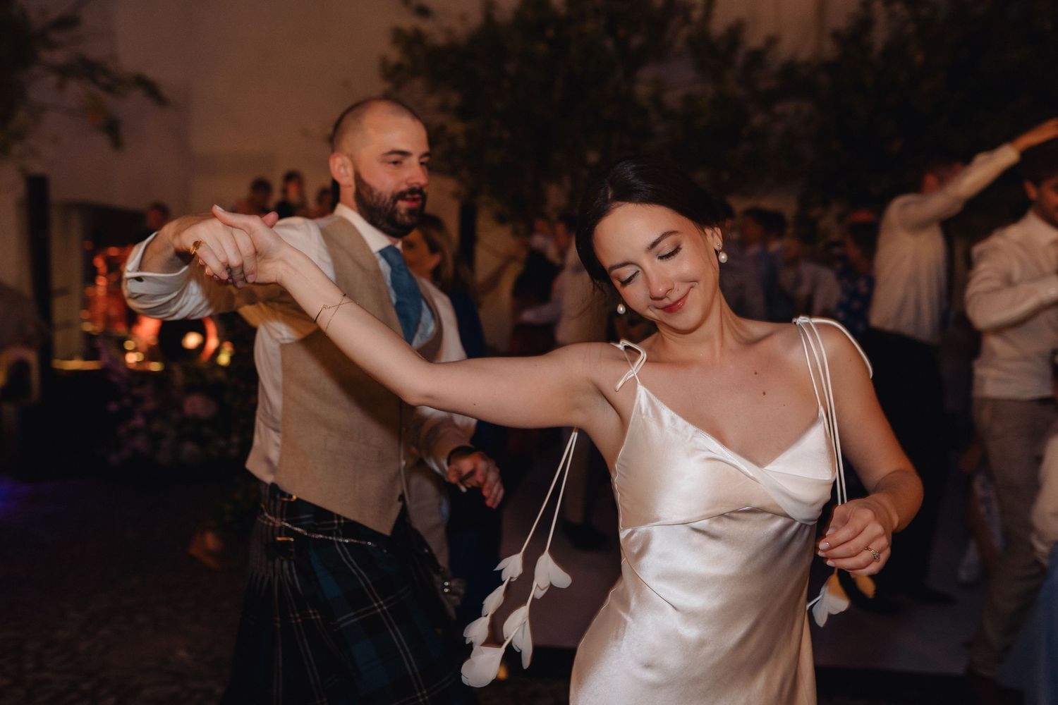 Wedding party dancing and celebrating during an evening reception with warm lighting.