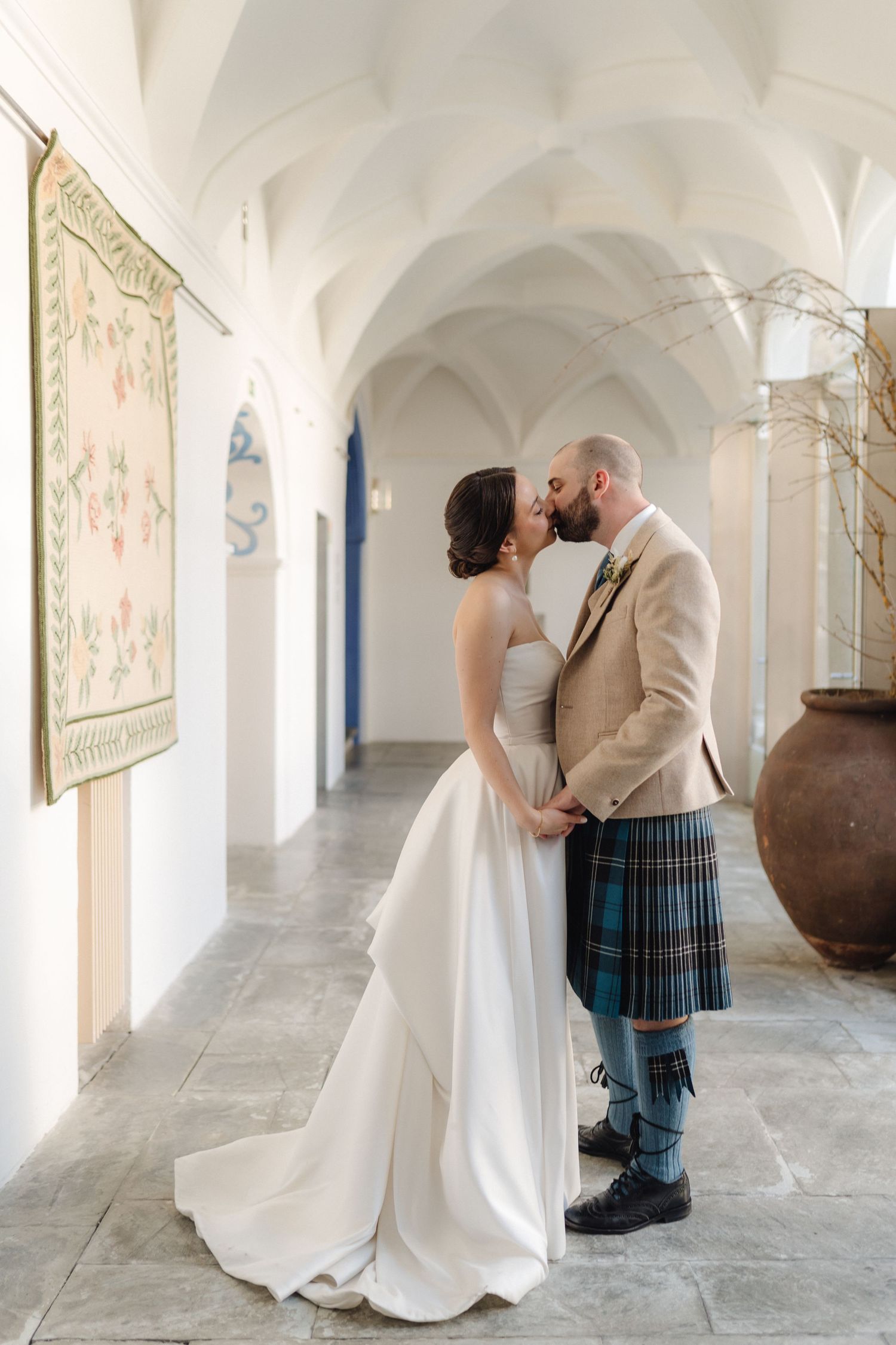 Wedding couple shares intimate moments in white arched hallway.