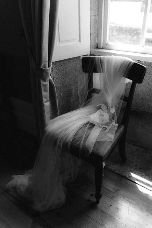 Wedding dress flowing over chair in dramatic window light.