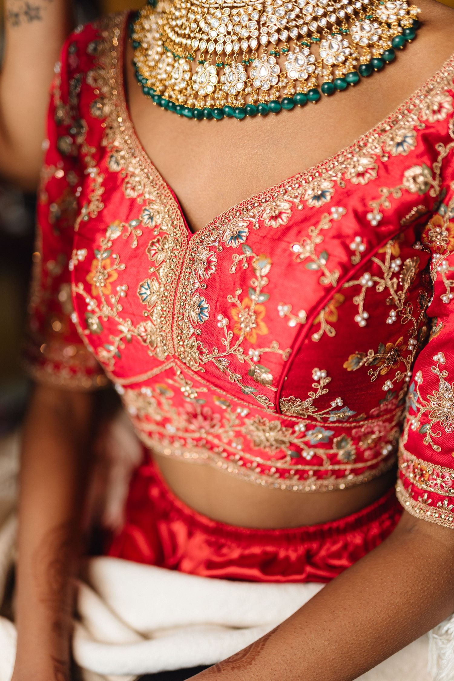 Close-up details of an ornate red and gold embroidered Indian bridal lehenga with jeweled embellishments.