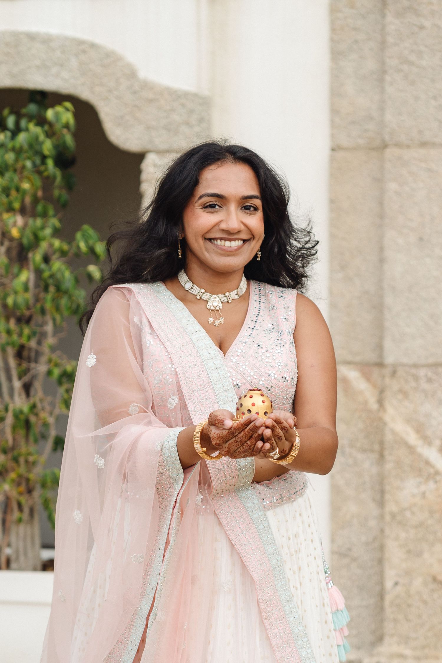 Person in white and pink traditional Indian attire poses joyfully against stone pillars.