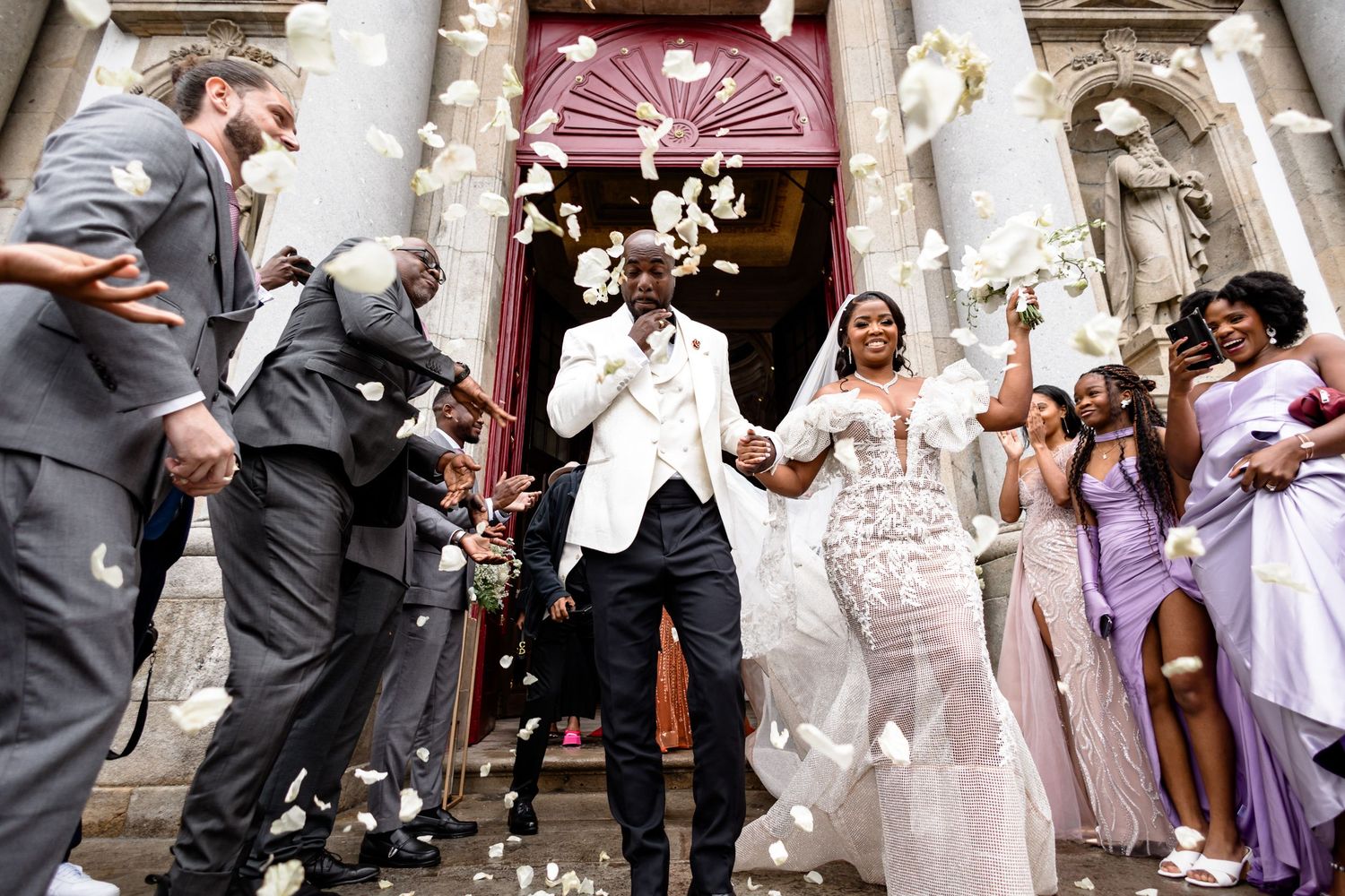 Newlyweds celebrating with guests as they exit church while rice and confetti are thrown.