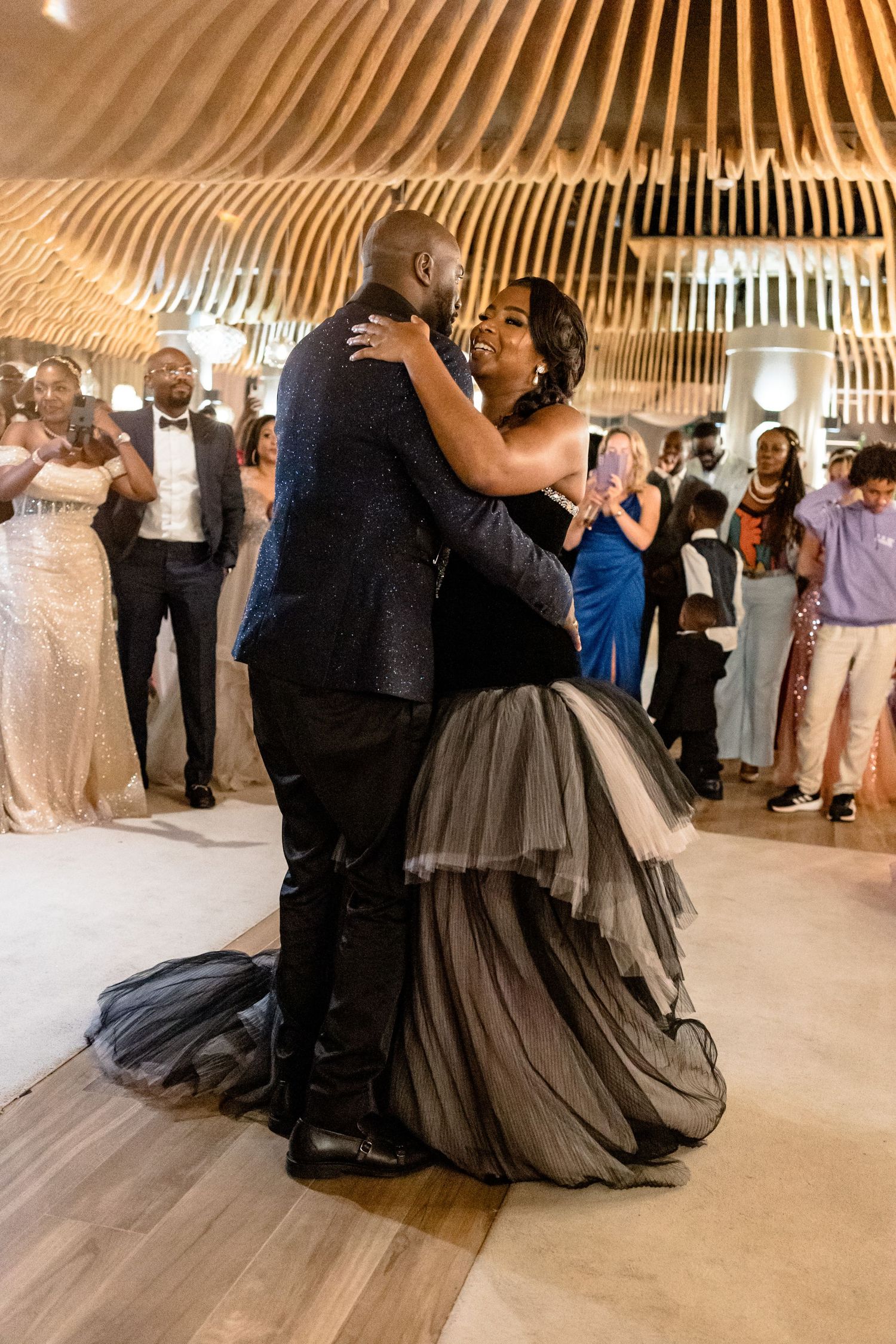 Couple sharing first dance under curved wooden ceiling at wedding reception.