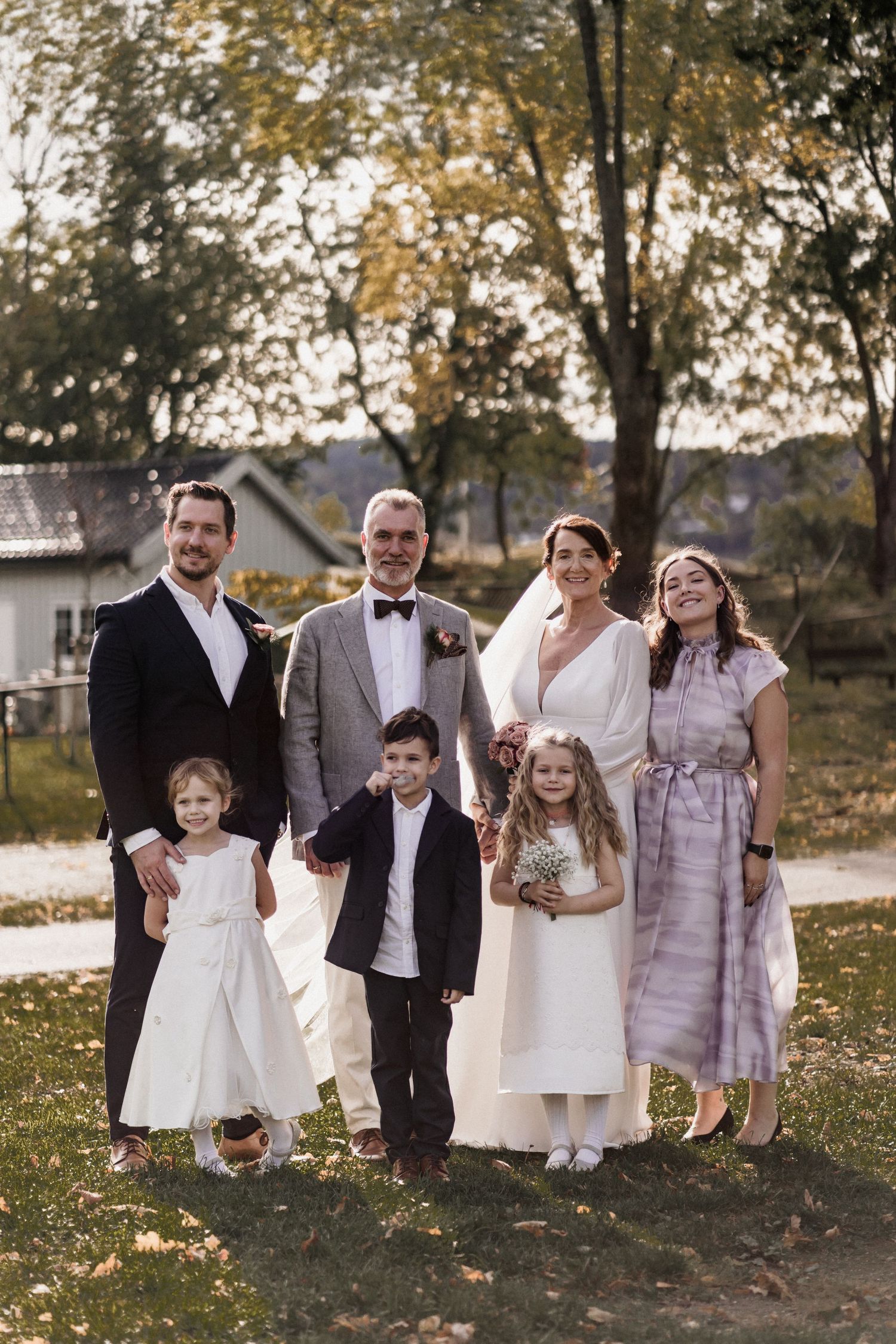 A group portrait of wedding party members in formal attire standing on an autumn lawn.