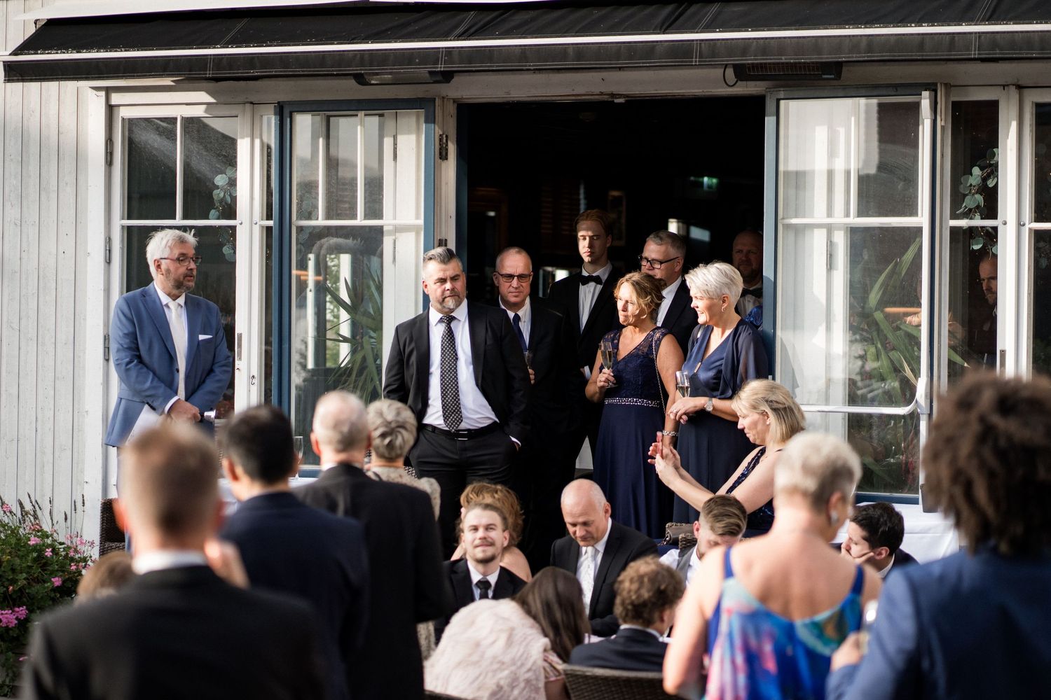 Wedding guests gathering outside a white building for a celebration.