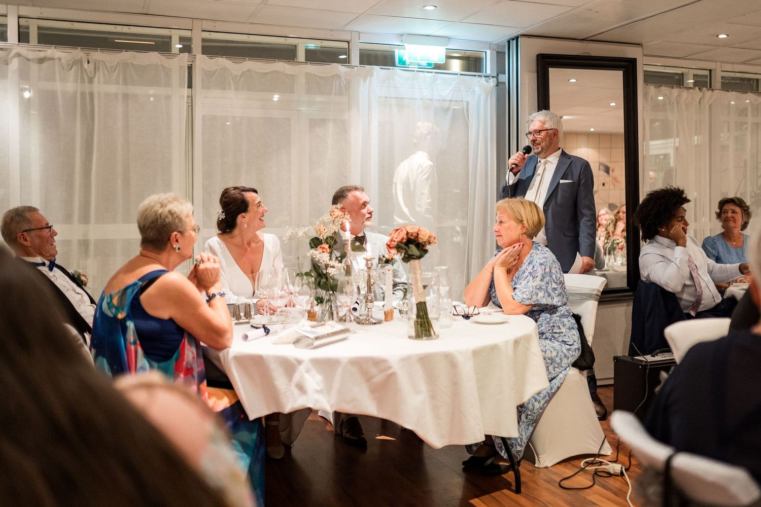 Formal dining event with white tablecloths and guests mingling in a well-lit restaurant space.