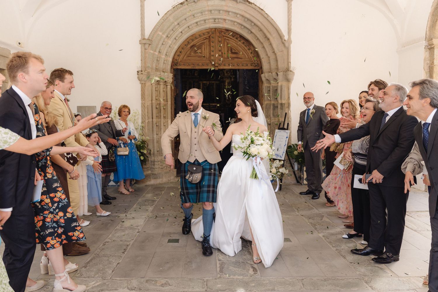 Wedding celebration in historic church corridor with guests and traditional Scottish attire.