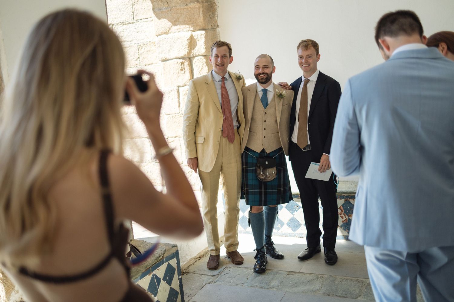 Wedding guests walking through a bright hallway with stone walls.