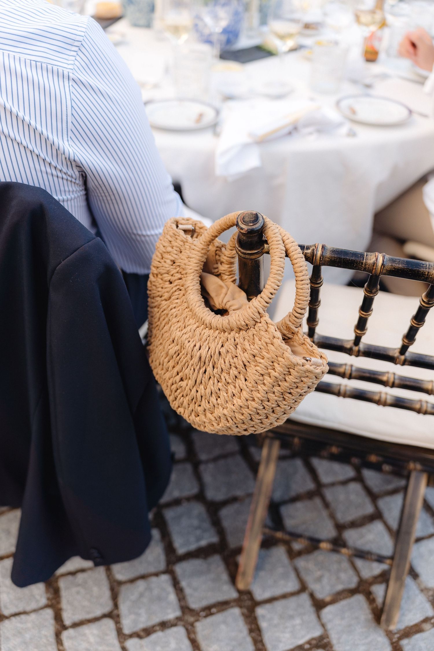 Straw handbag resting on a wooden chair at an outdoor event setting.