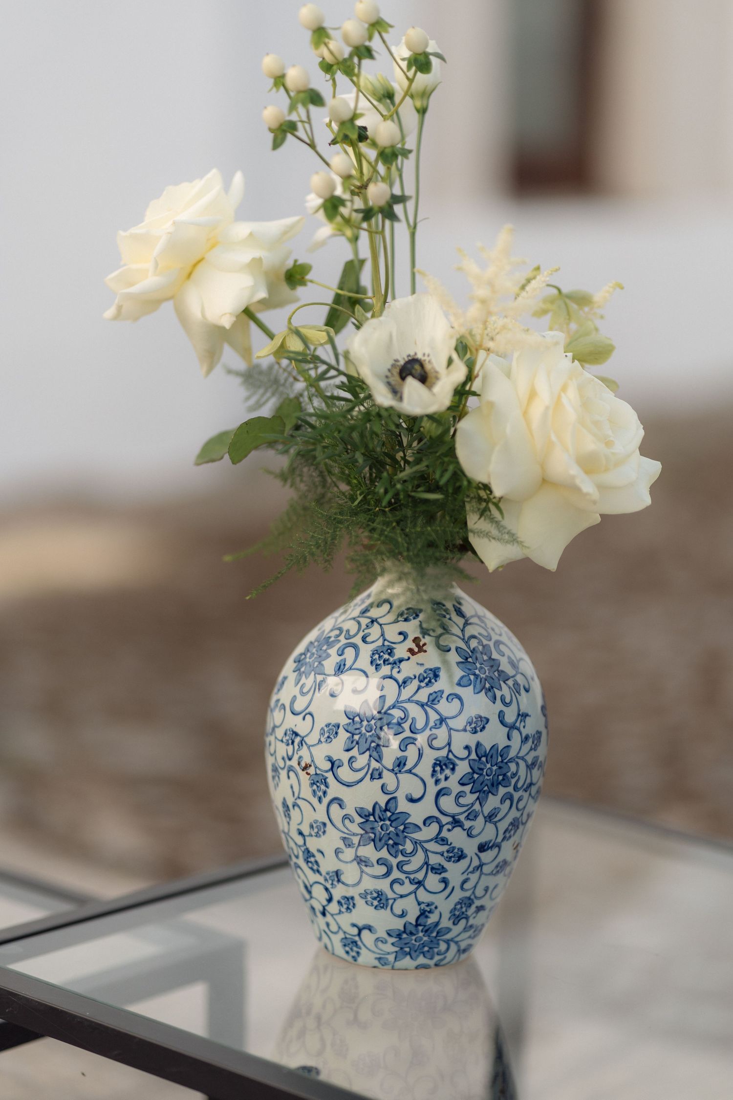 White roses arranged in a blue and white chinoiserie vase displayed on a glass surface.