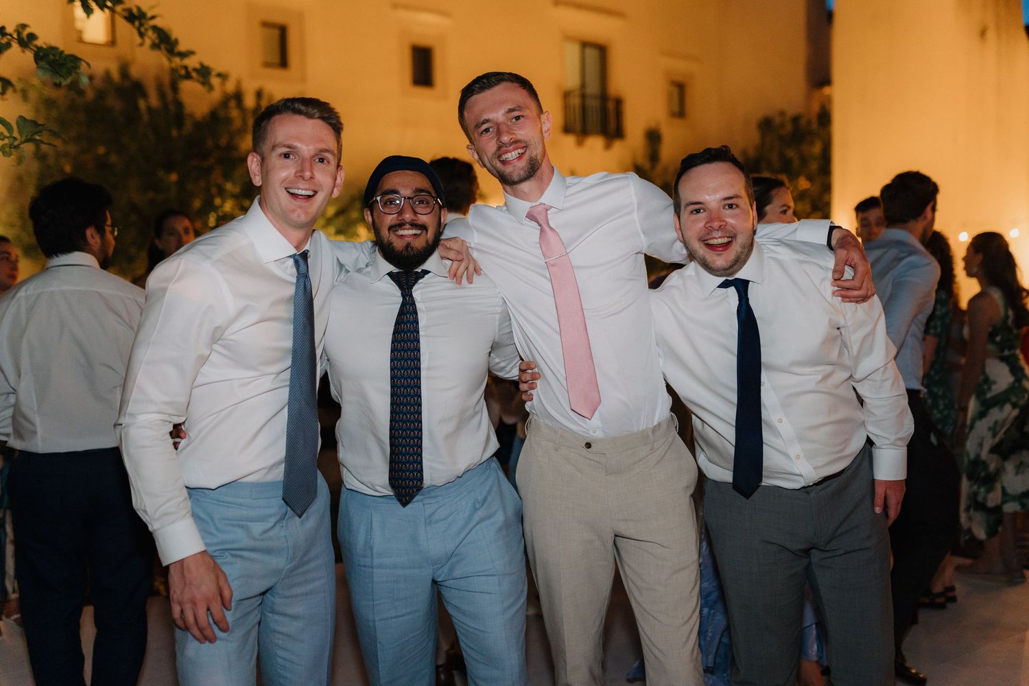 Groomsmen in light blue and tan suits posing together at an outdoor wedding venue.