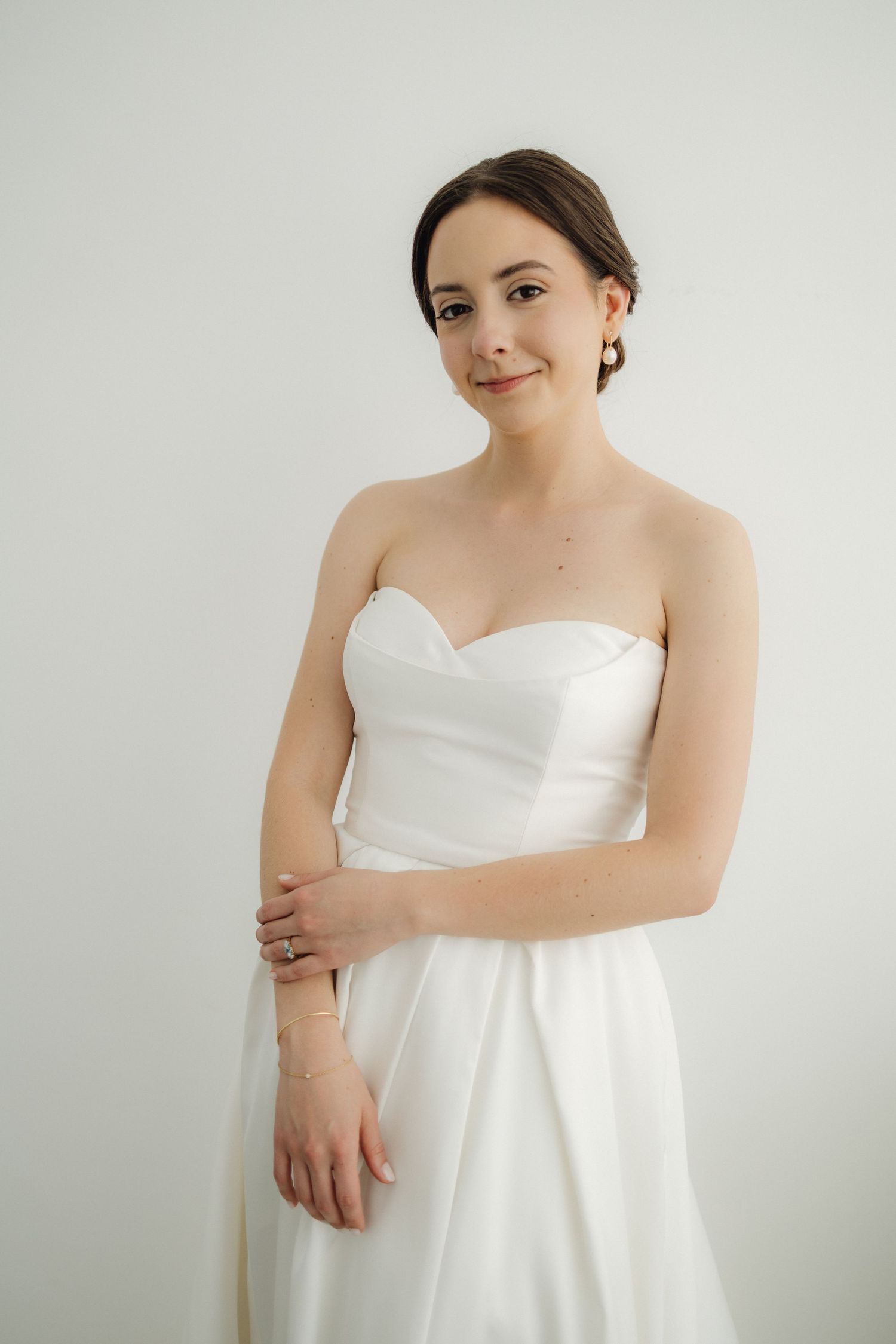 Bride in strapless white dress poses elegantly against white backdrop.
