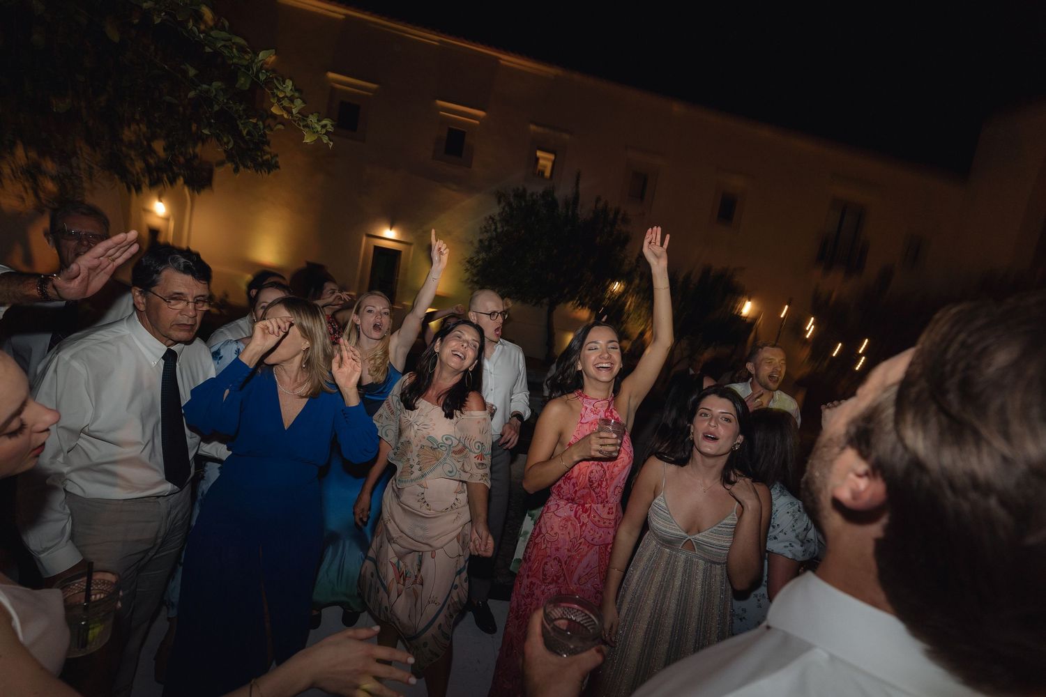 Enthusiastic wedding guests dancing and celebrating at a nighttime outdoor reception.
