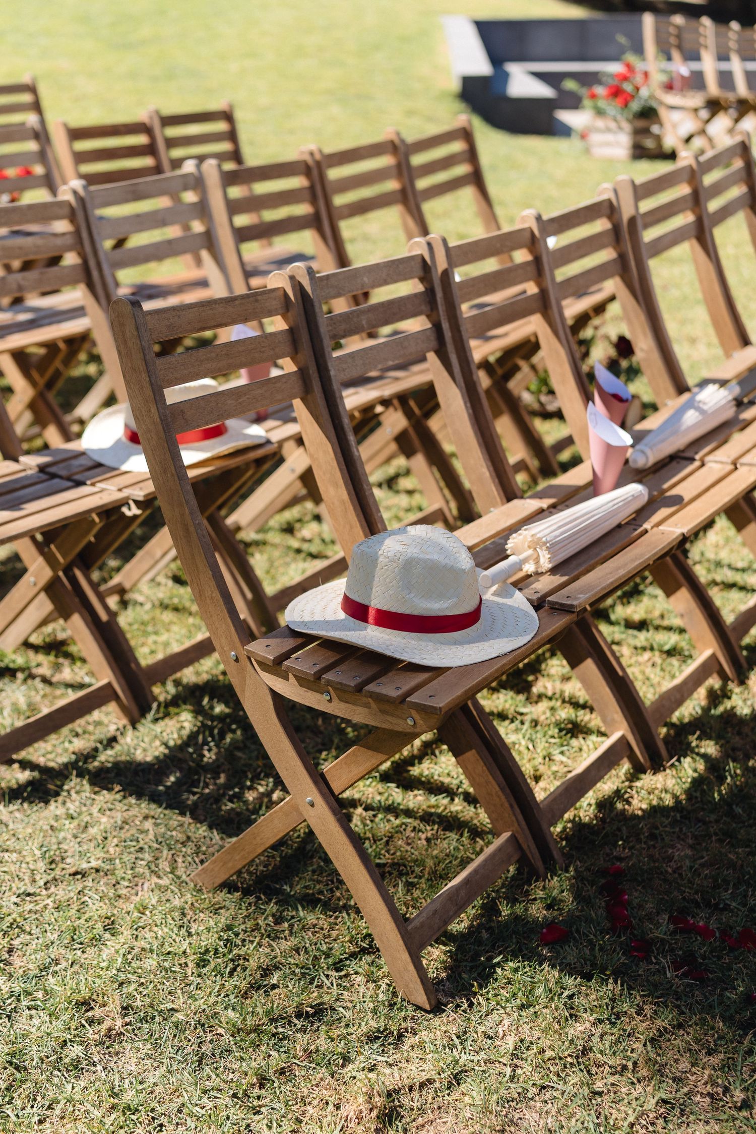 Wooden folding chairs lined up on grass with white sun hats placed on seats.
