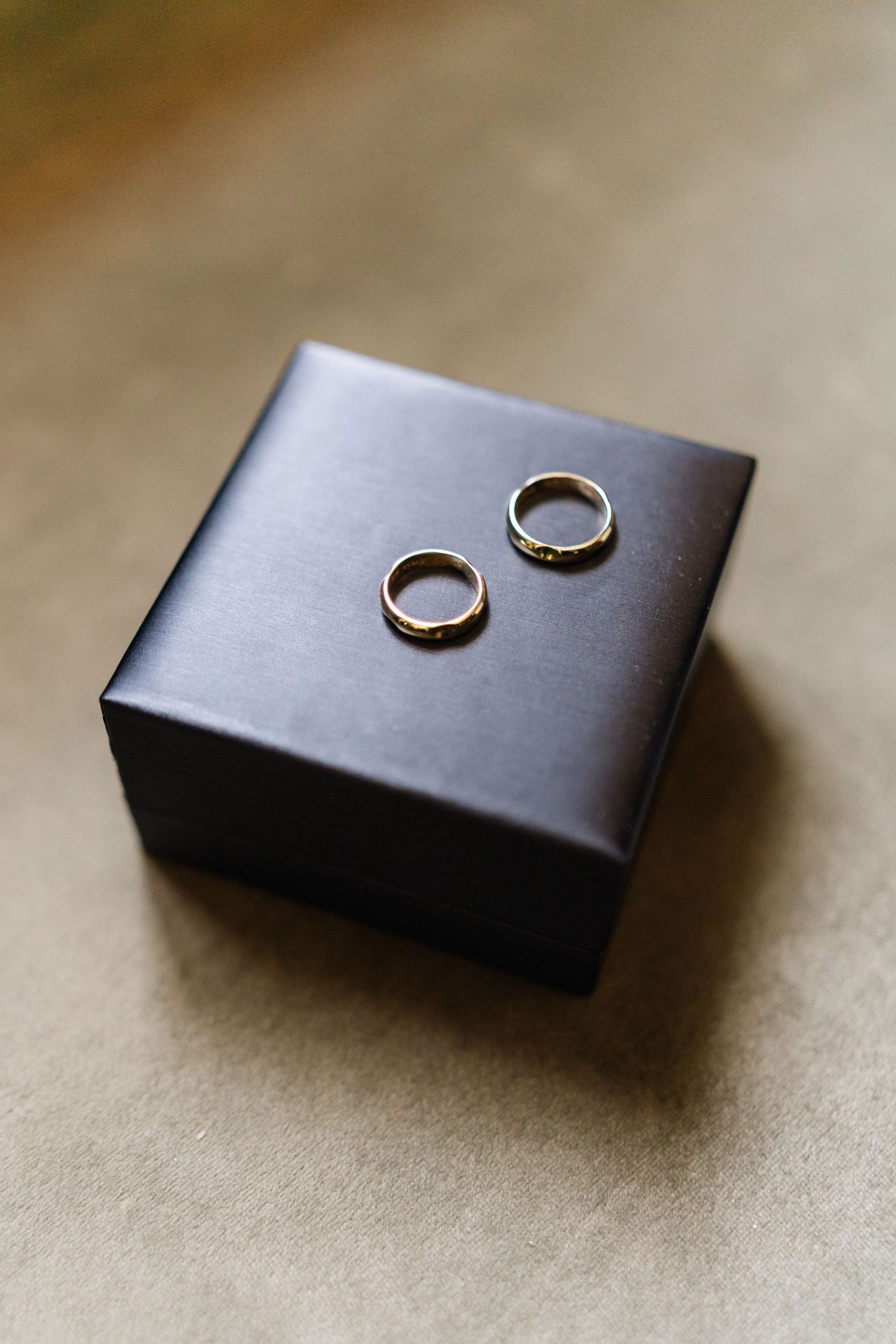 Two wedding rings placed on a dark leather box against neutral background.