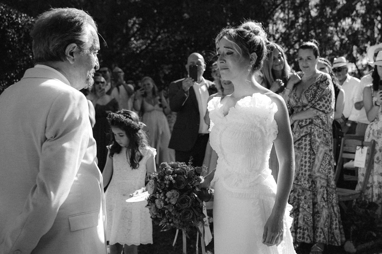 Black and white photo of wedding guests reacting emotionally during outdoor ceremony.