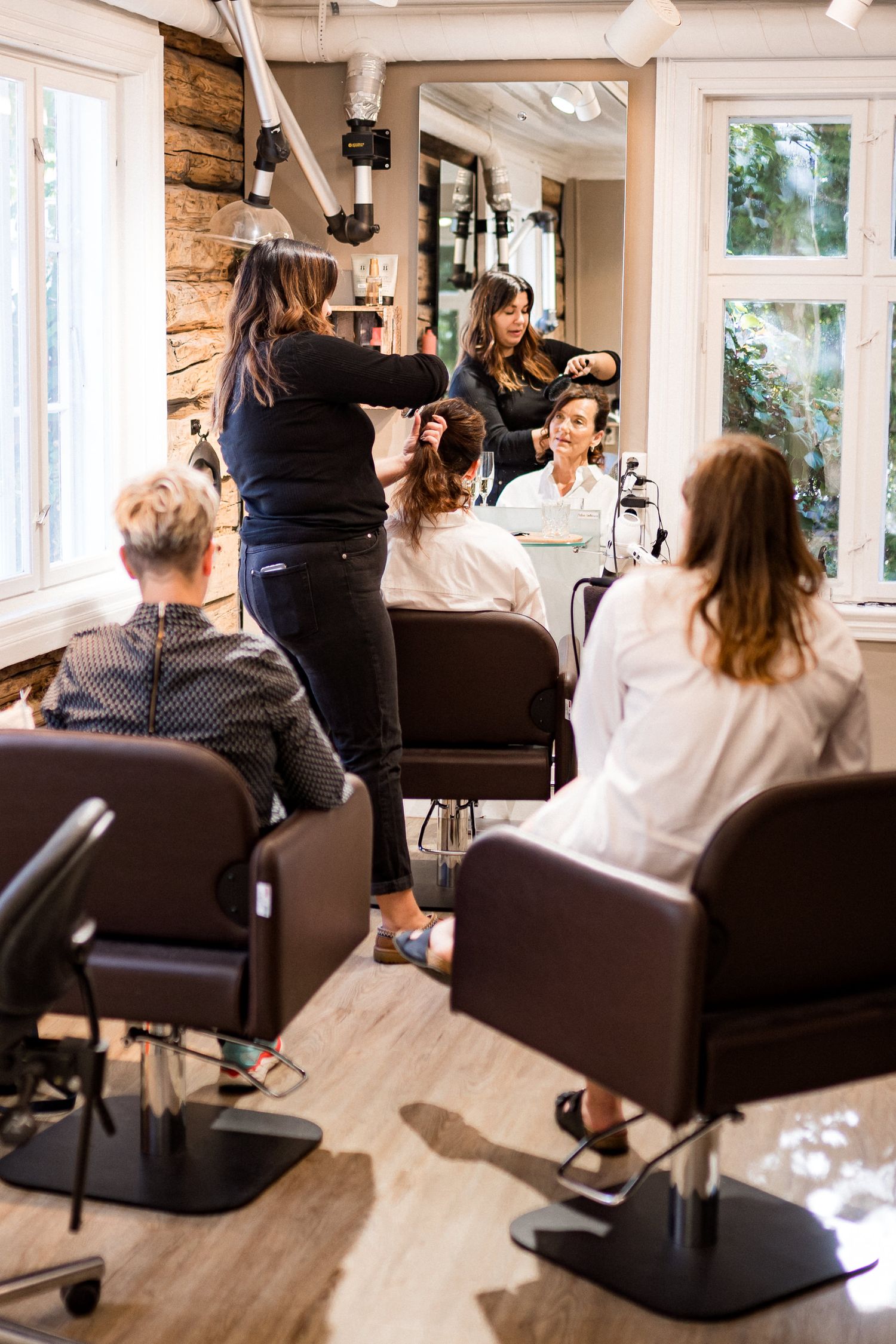 Wedding guests seated in brown chairs at a salon venue with natural lighting through windows.